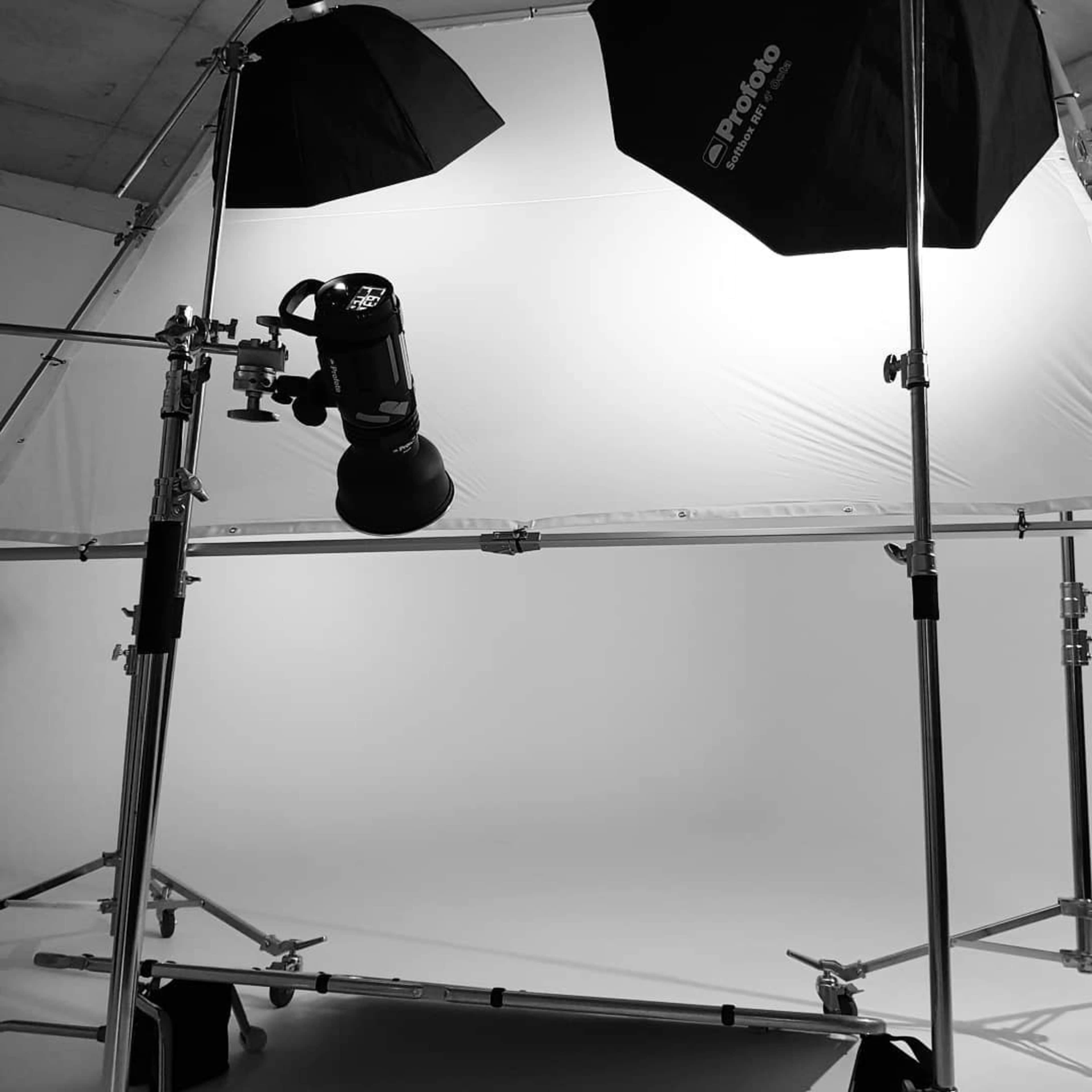 A photography studio setup featuring a light source mounted on a support frame with softboxes and a seamless backdrop.