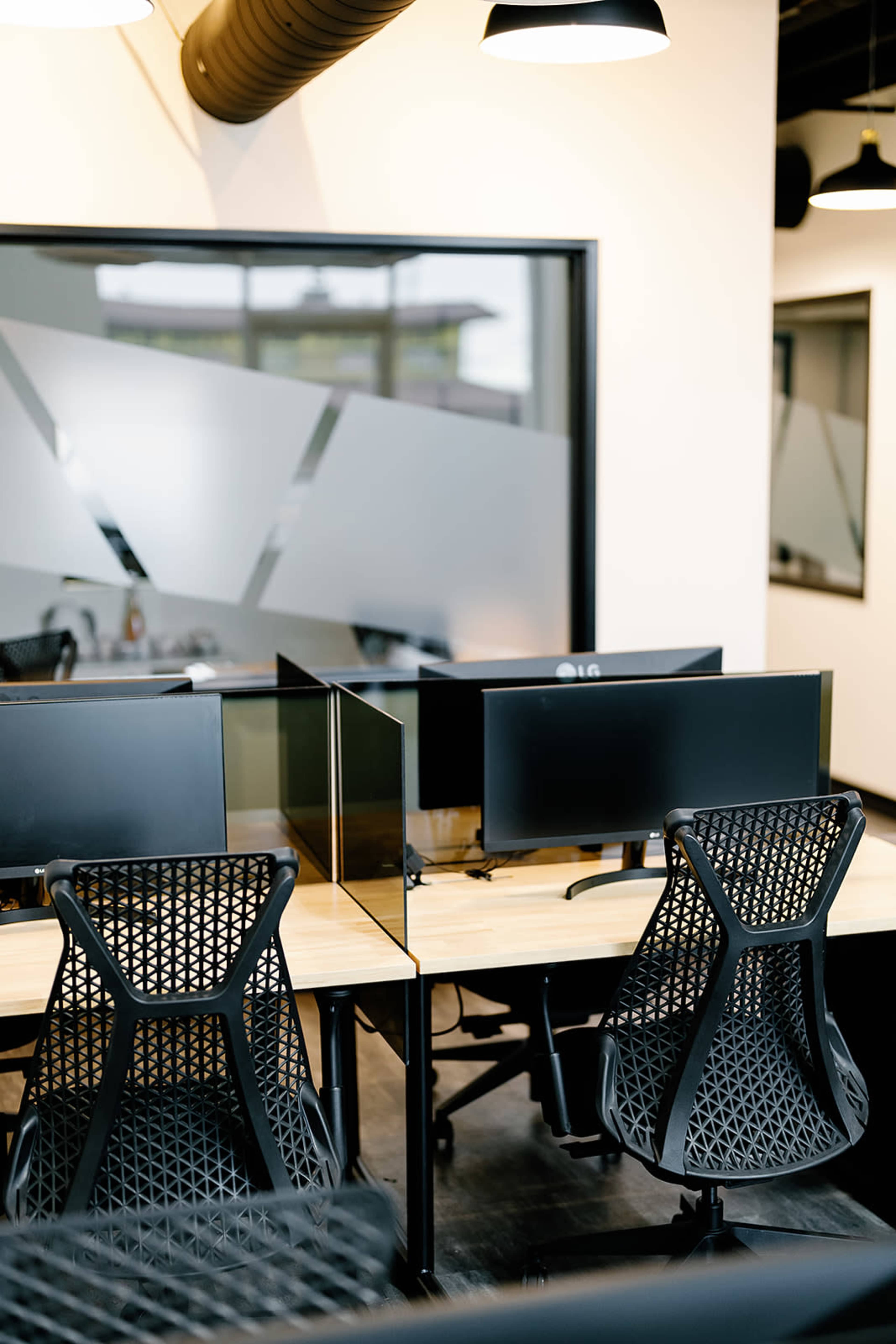 An office space with several empty desks, each equipped with a computer monitor and black mesh office chairs.