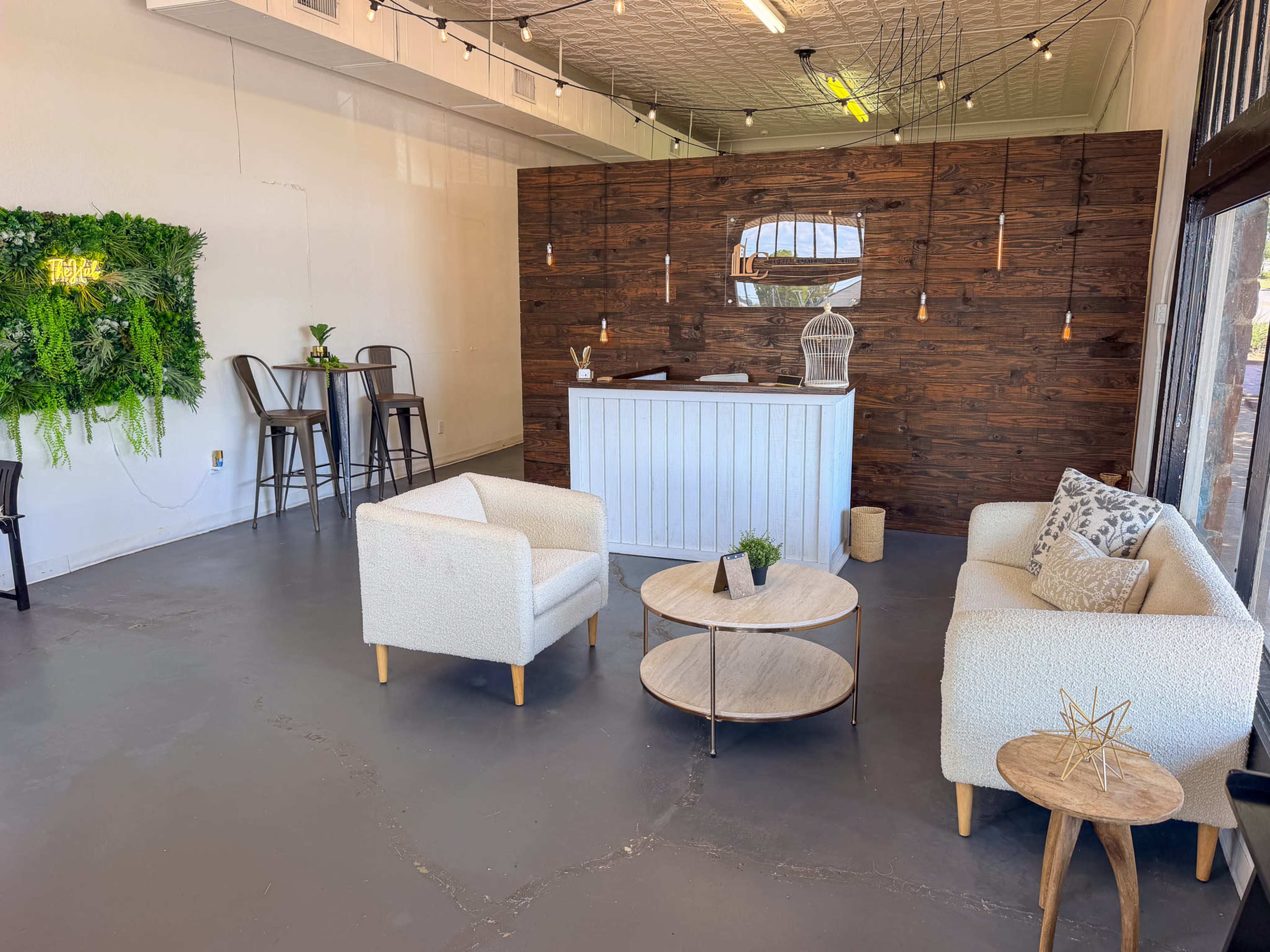 The image shows a spacious, minimalist interior with a reception area featuring a wooden desk, two white chairs, and a small coffee table on a concrete floor.