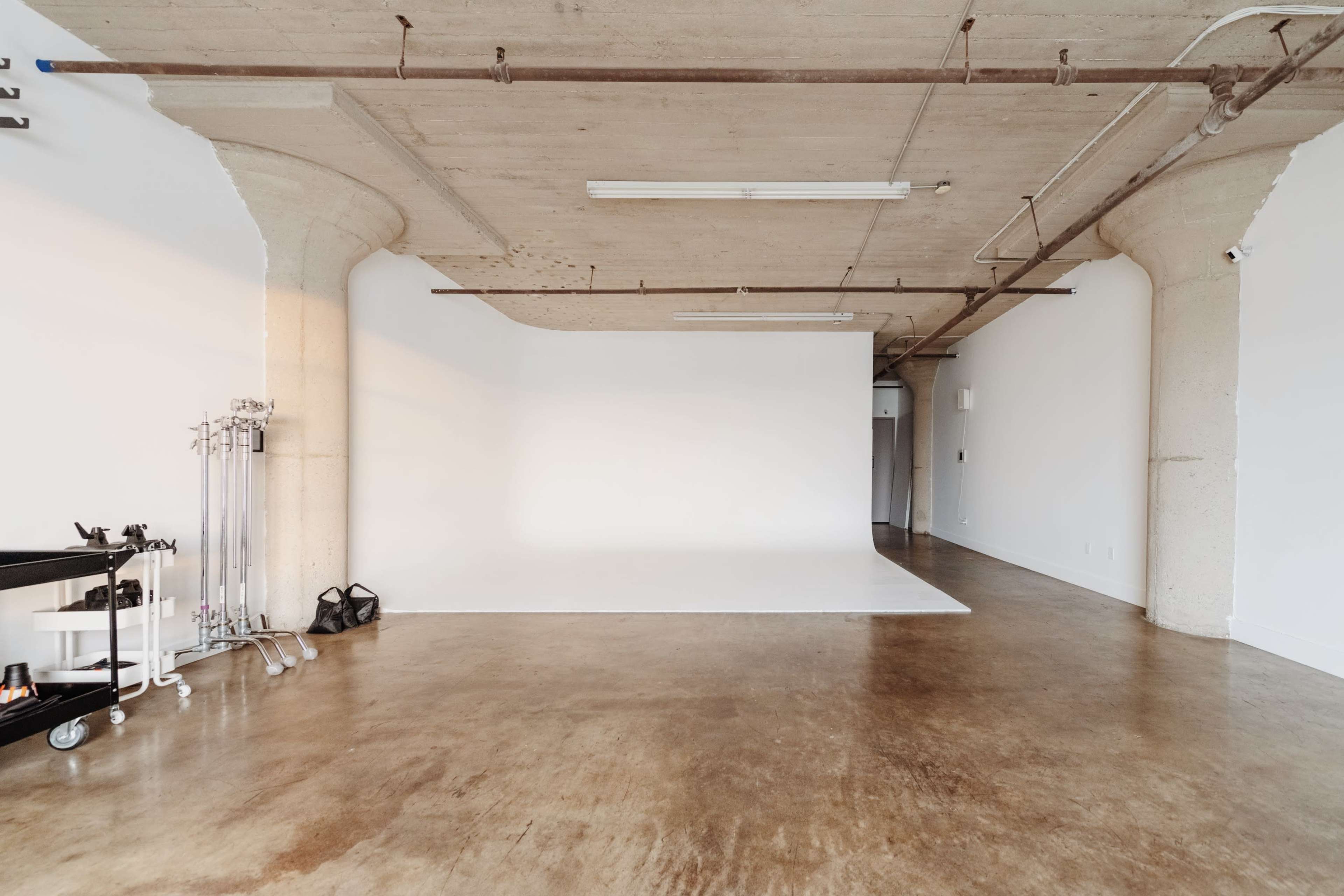 A spacious, empty studio with a white backdrop and polished concrete floors.
