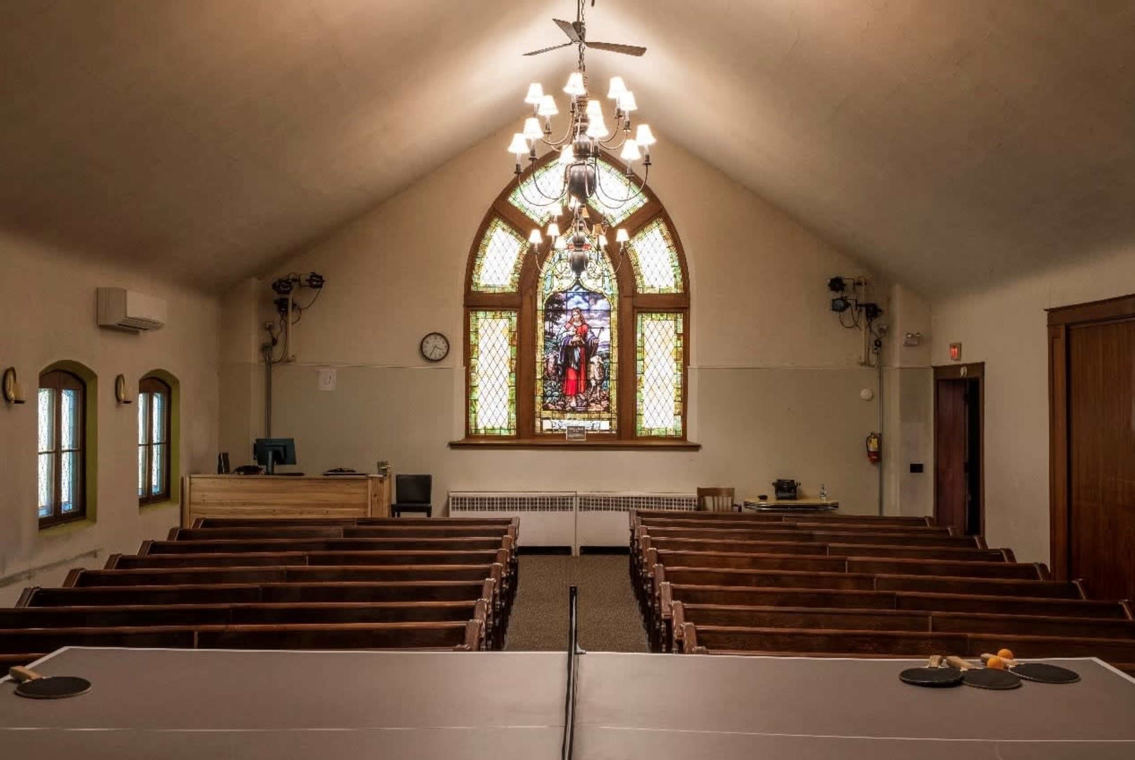 The image shows the interior of a church with wooden pews facing a stained glass window at the front.