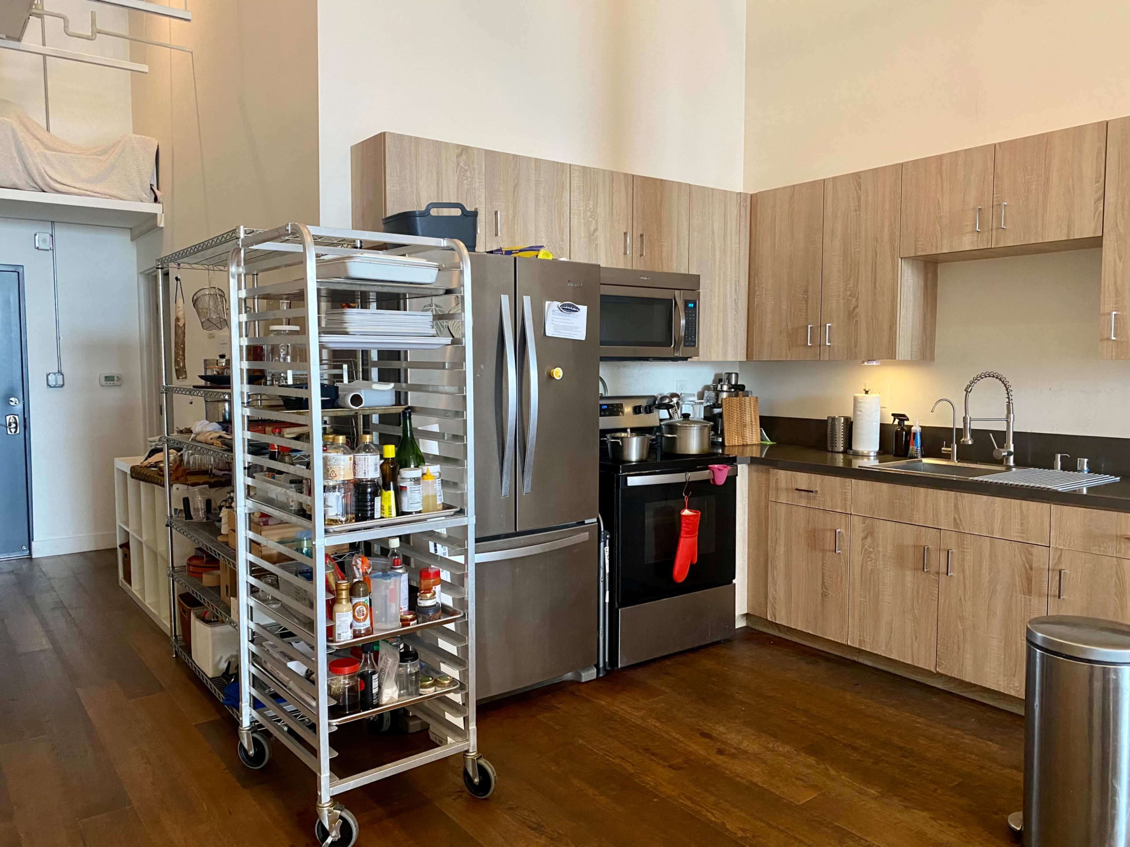 A modern kitchen features stainless steel appliances, wooden cabinetry, and a mobile shelving unit filled with various cooking supplies.