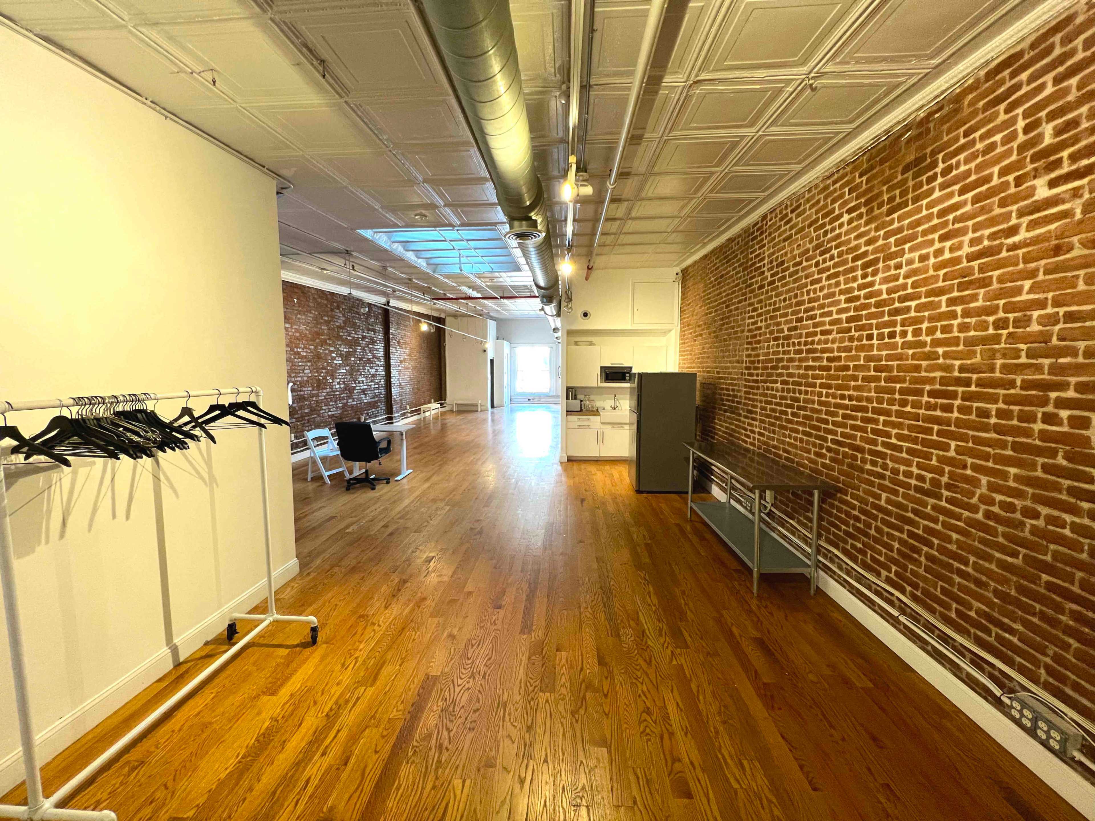 A spacious interior with hardwood floors, exposed brick walls, and a kitchen area at the far end.
