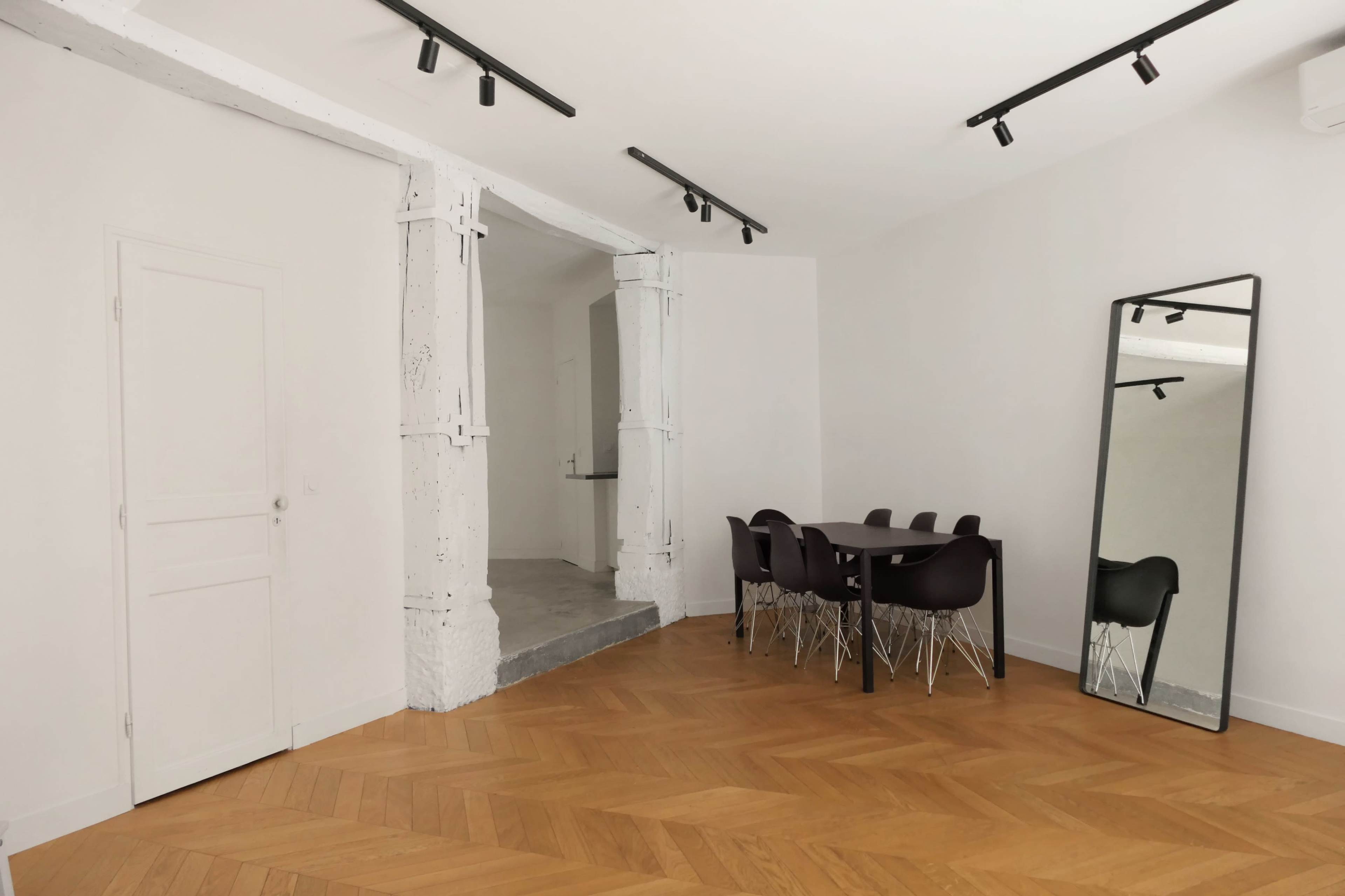 A dining area features a wooden table surrounded by black chairs, with a large mirror and a doorway leading to another room.