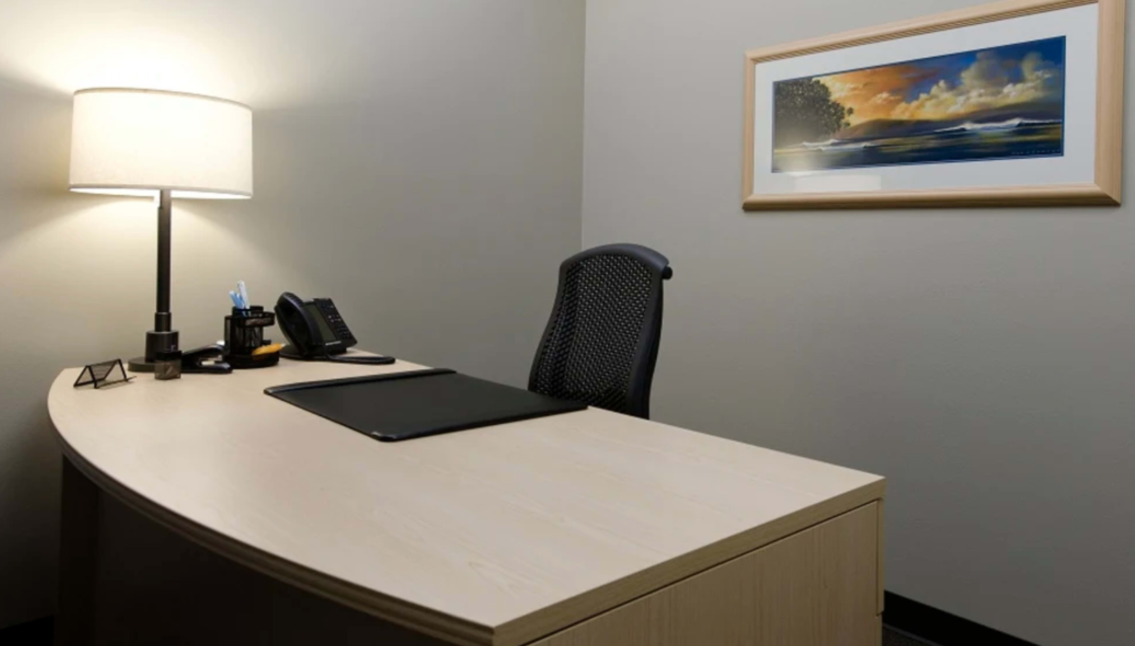 The image shows a minimalist office space featuring a desk with a lamp, a phone, and a framed landscape painting on the wall.