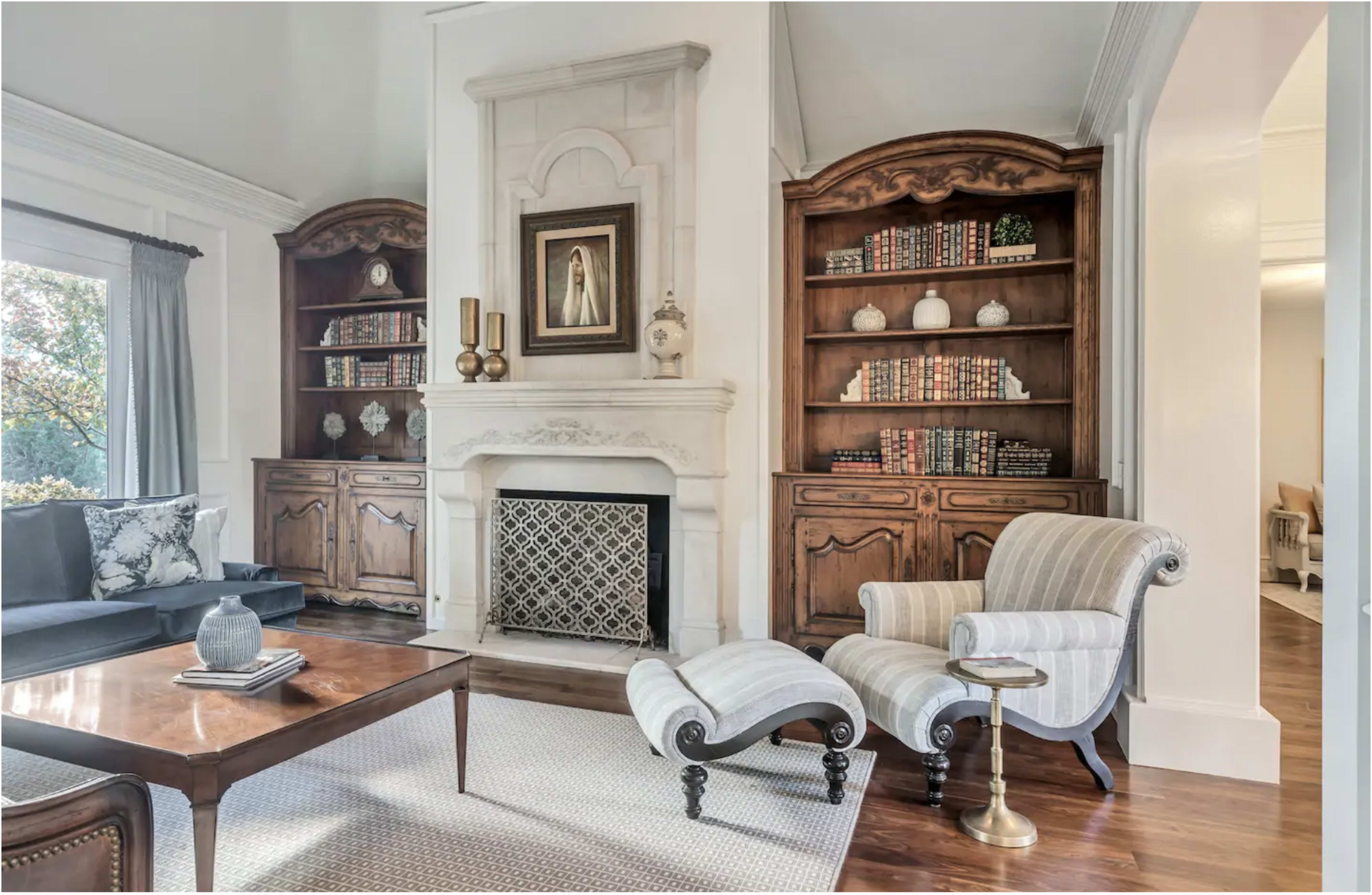 A living room featuring a fireplace with a decorative mantel, built-in bookshelves, a striped armchair, and a wooden coffee table.