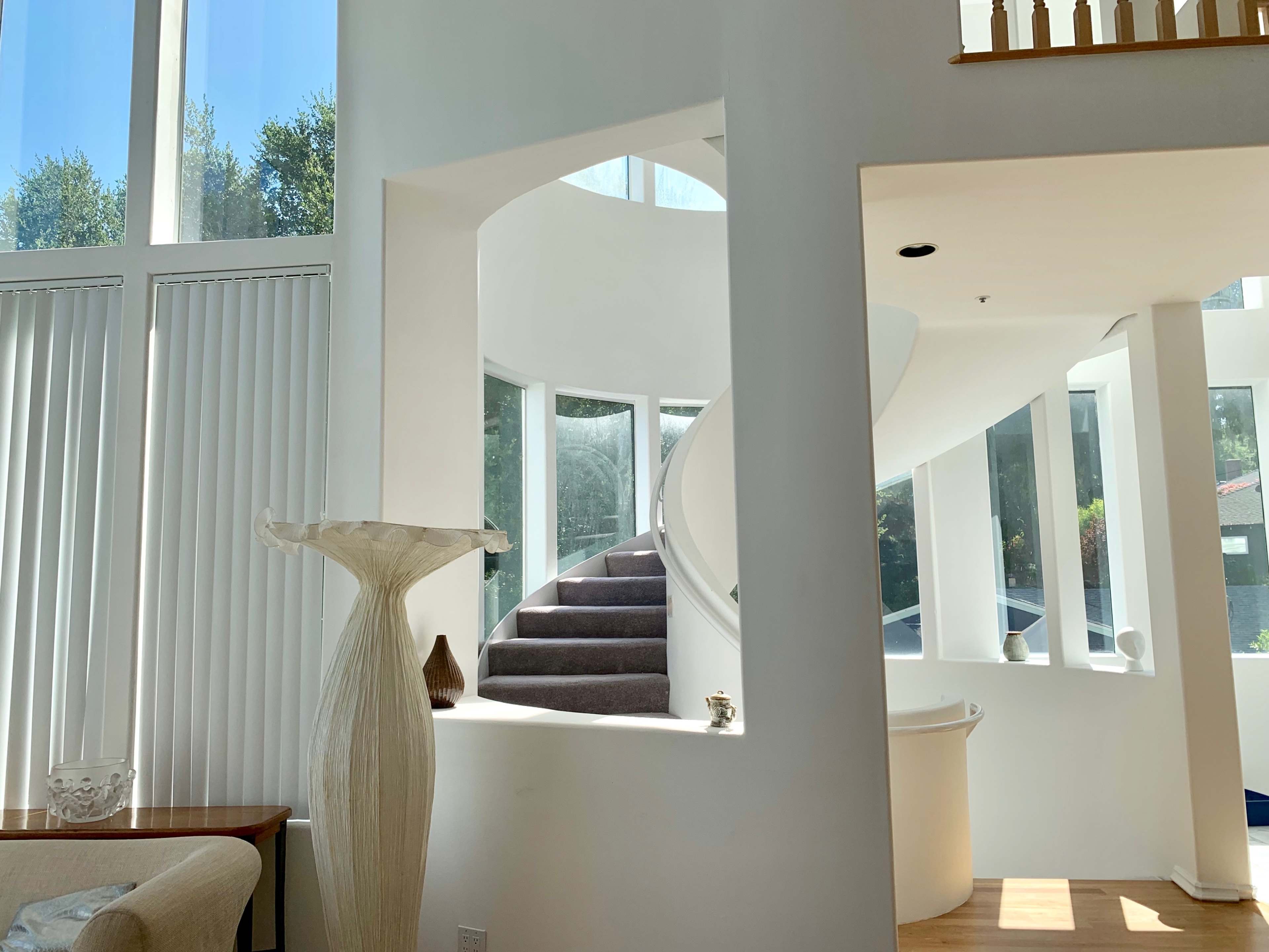 A bright interior with a spiral staircase leading to an upper level, surrounded by large windows that let in natural light.