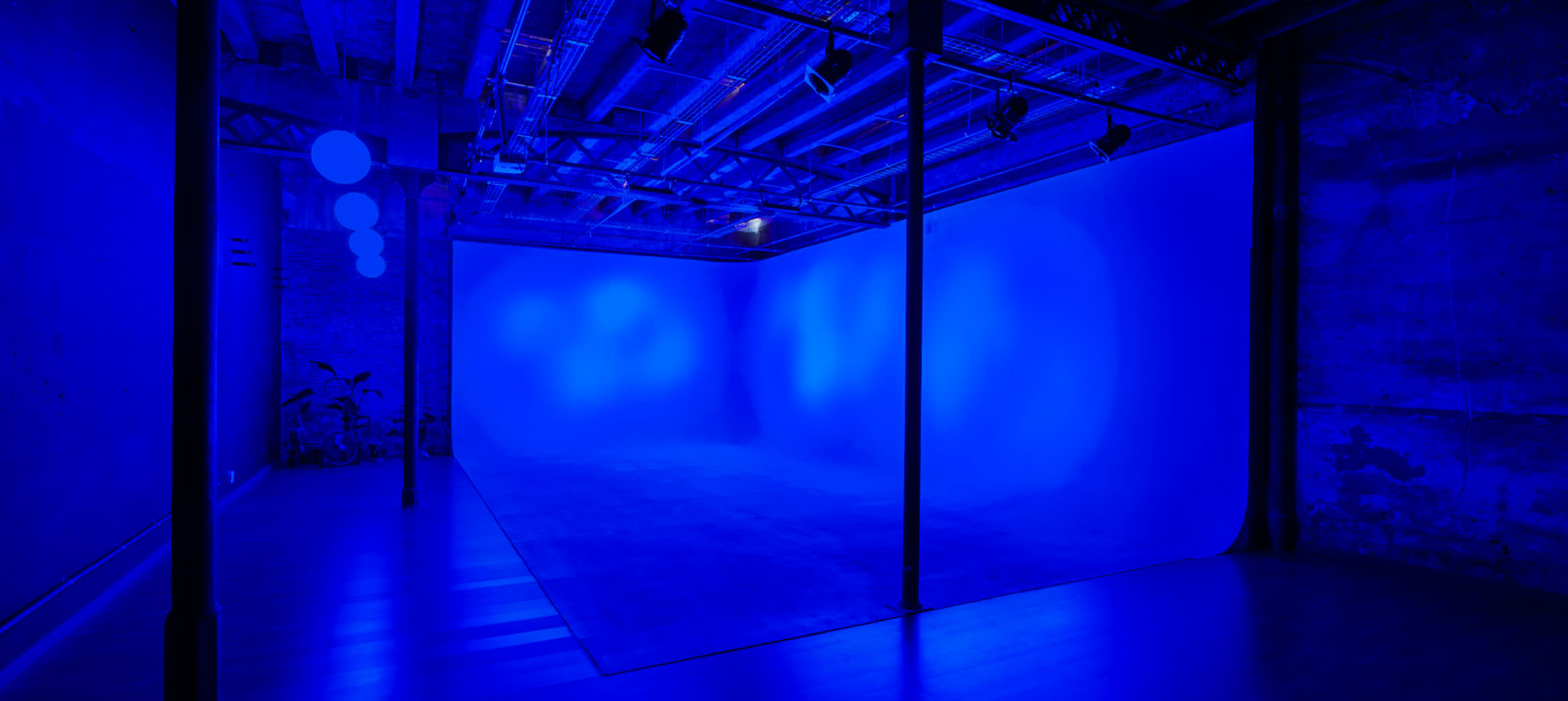 An empty studio space with blue lighting, featuring a seamless backdrop and exposed ceiling beams.