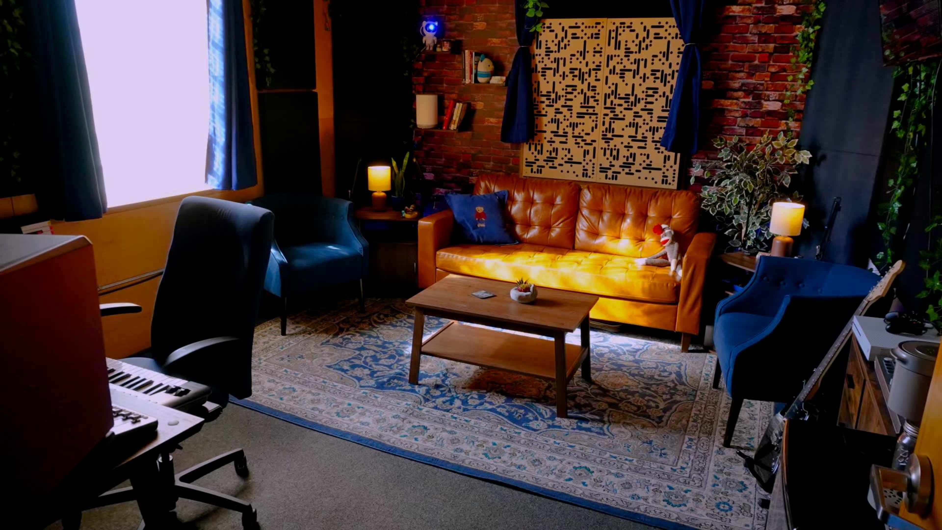A cozy living room with a brick wall, orange sofa, blue chairs, a coffee table, and a patterned rug under soft lighting.
