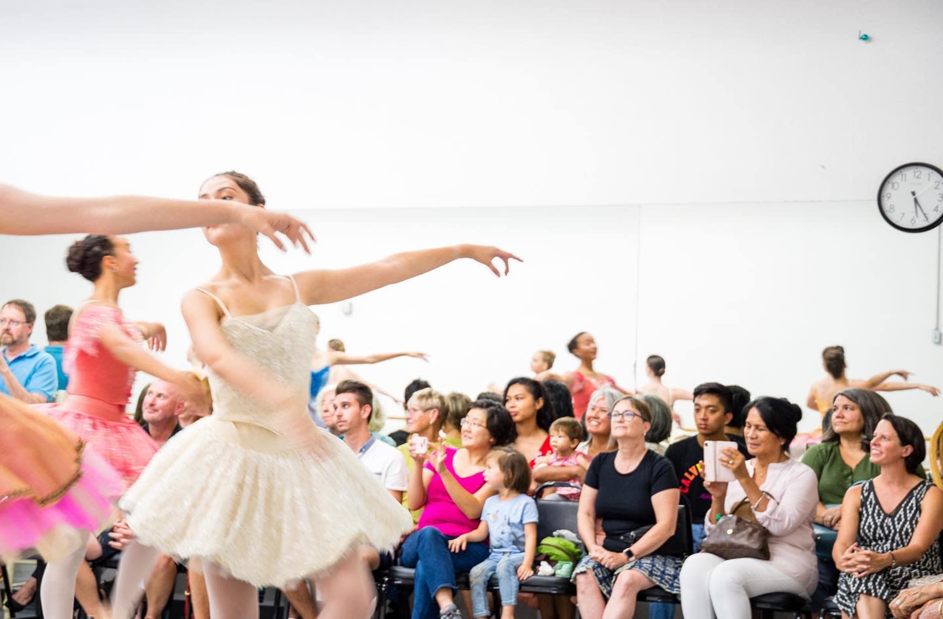 A group of people watch dancers in tutus perform in a dance studio.