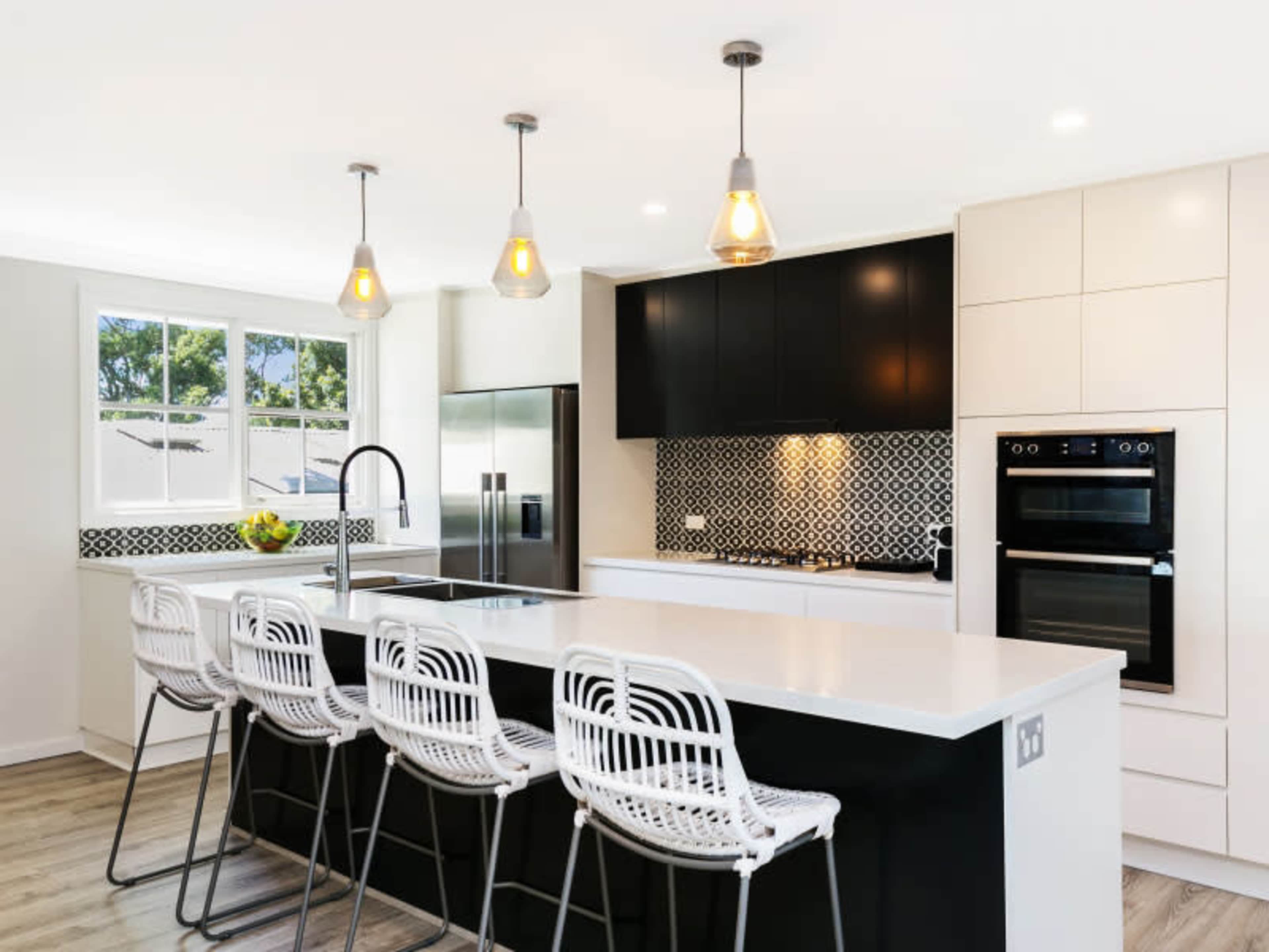 A modern kitchen with a large island featuring bar stools, sleek cabinetry, and decorative tile backsplash.