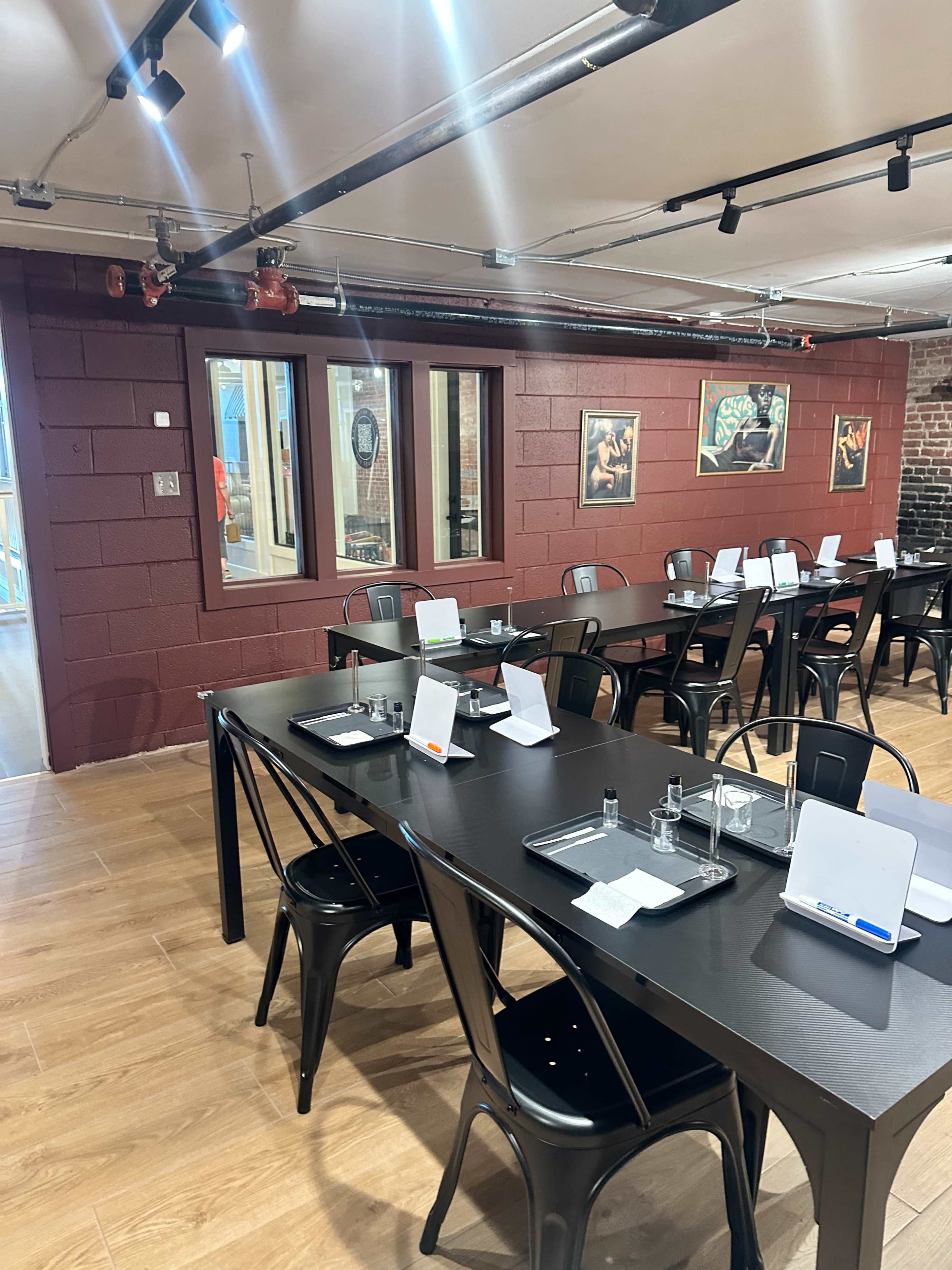 The image shows a spacious restaurant interior featuring black tables and chairs, with a maroon accent wall adorned with framed artwork.
