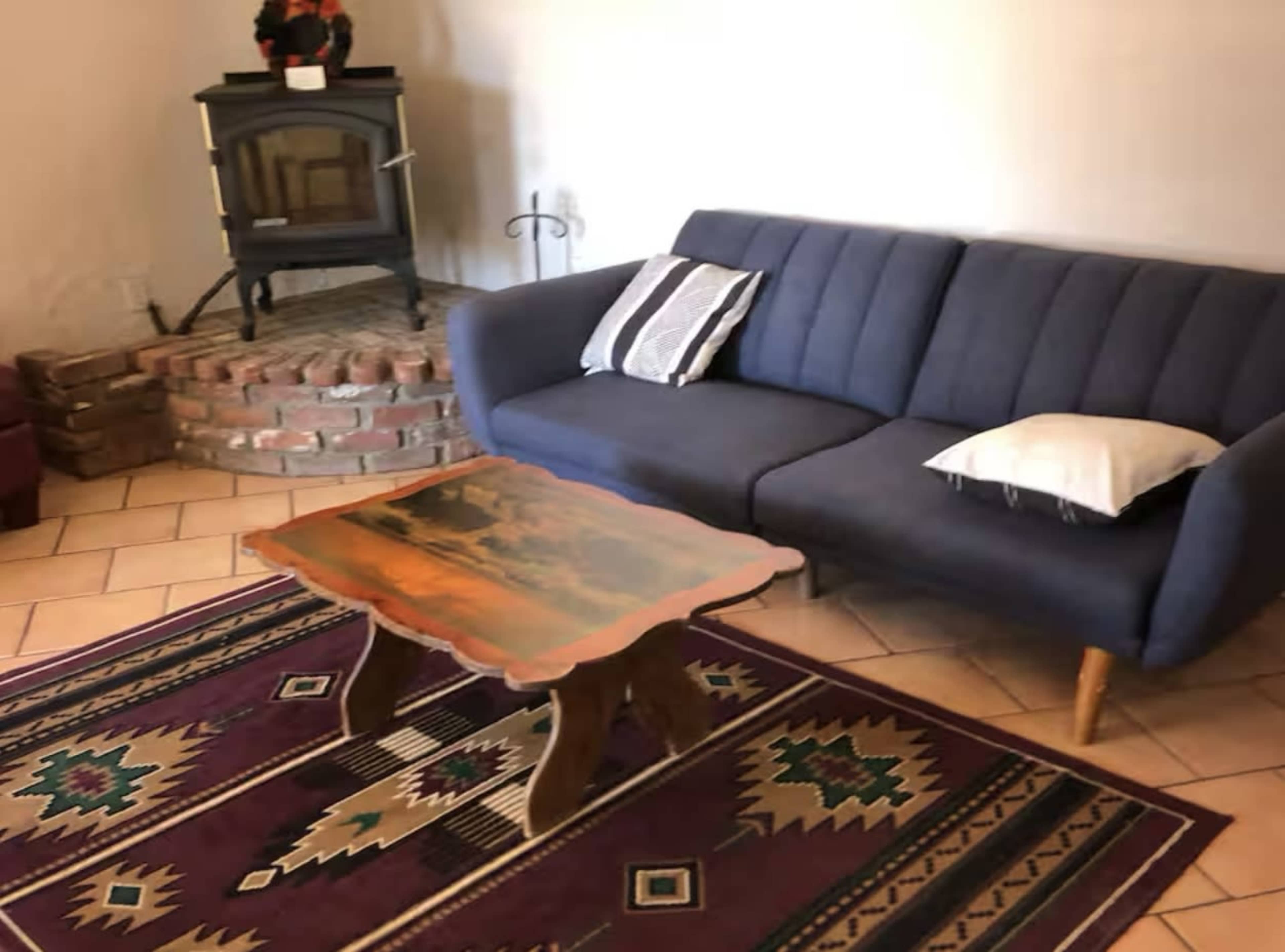 The image shows a living room with a blue couch, a wooden table with a scenic tabletop, and a brick fireplace in the background.