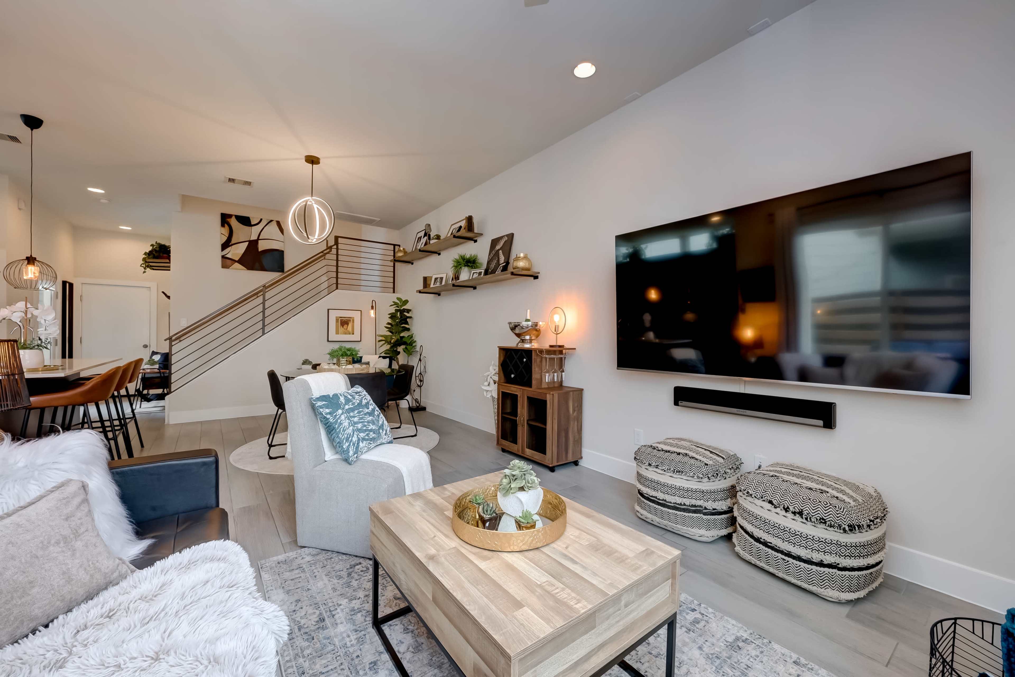 A modern living room with a large television mounted on the wall, a coffee table in the center, and a staircase leading to an upper level.