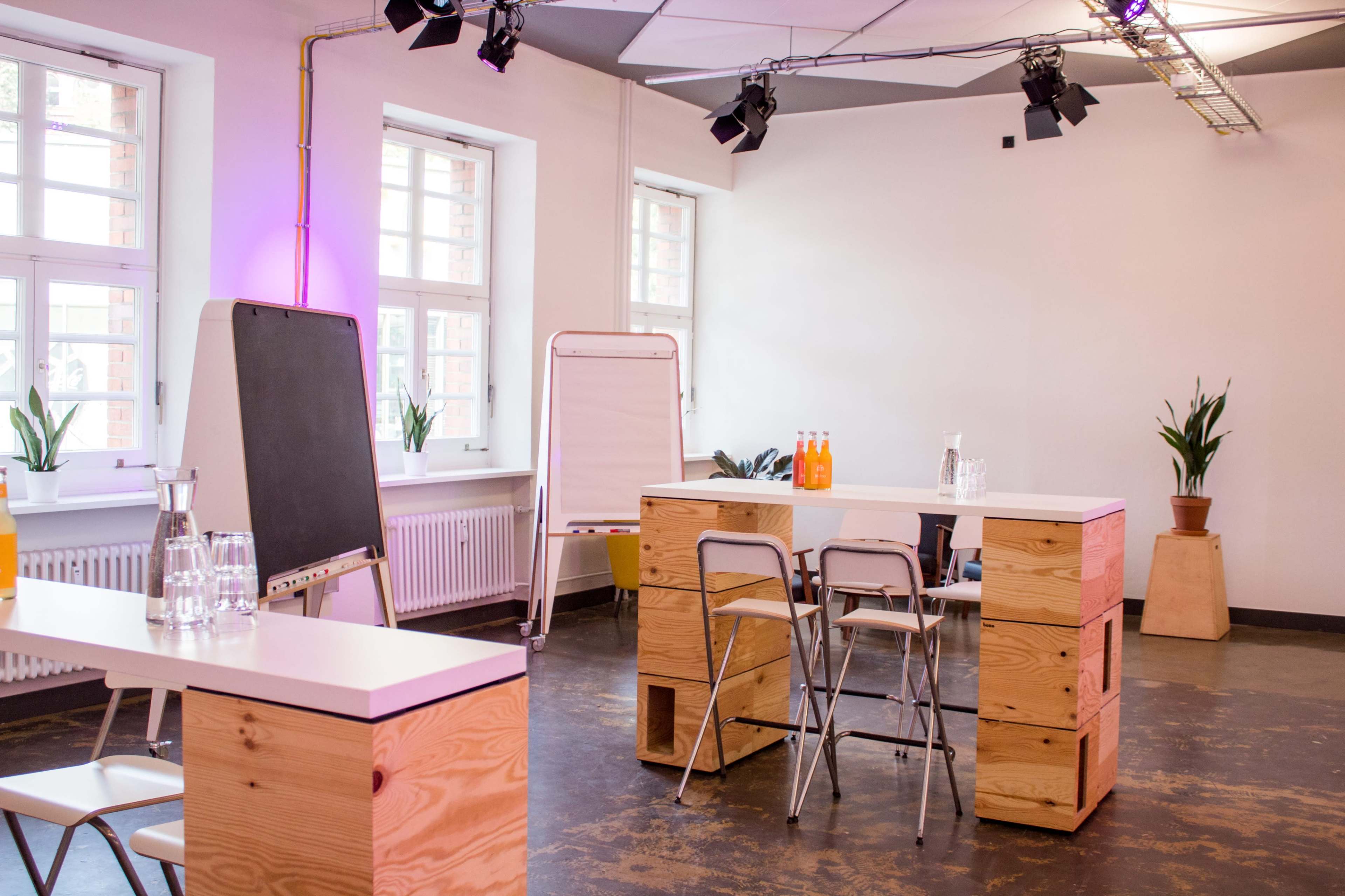 A spacious, modern meeting room features wooden furniture, a chalkboard, and large windows with plants nearby.
