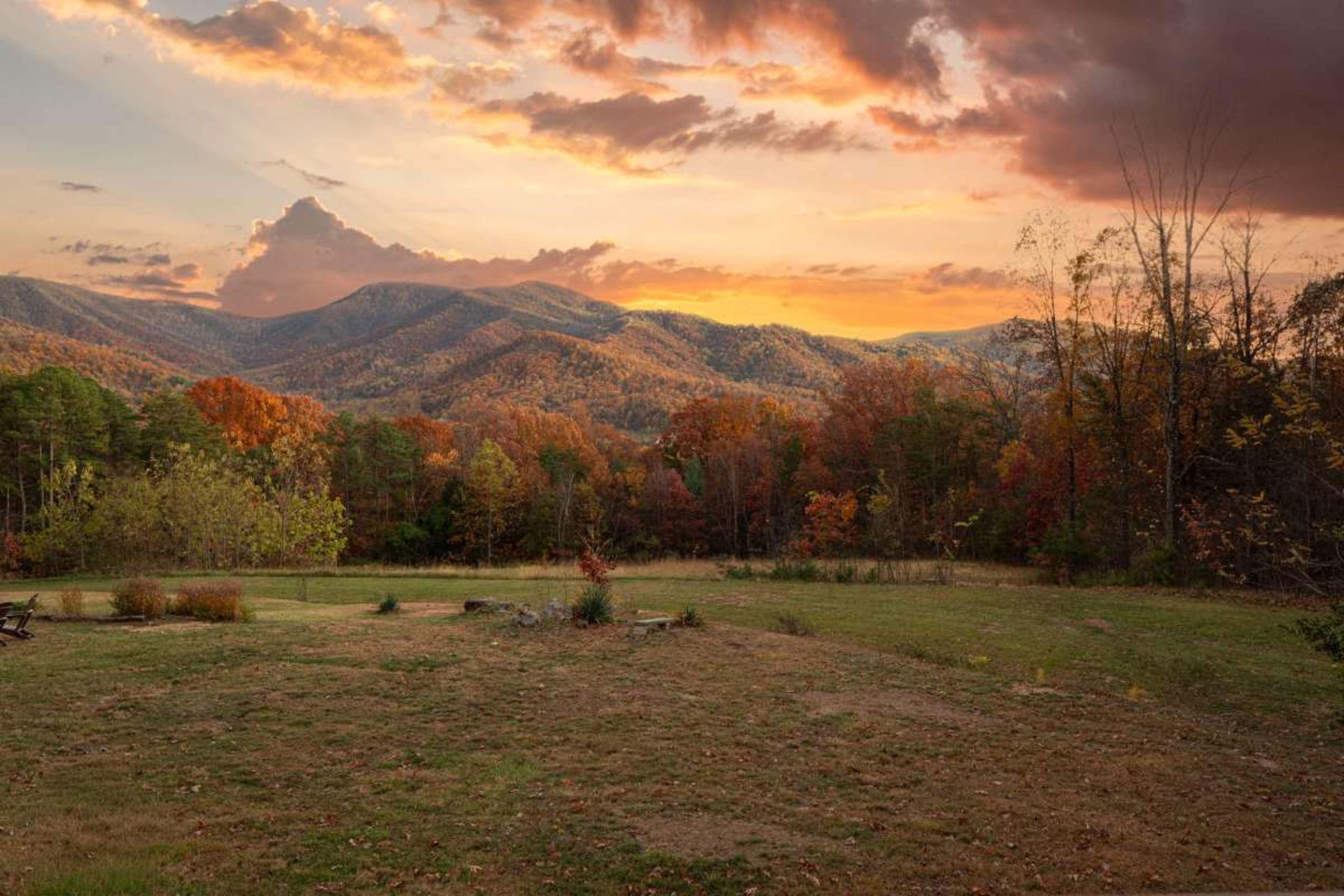 The image shows a scenic view of mountains during sunset, with trees displaying autumn colors in the foreground.