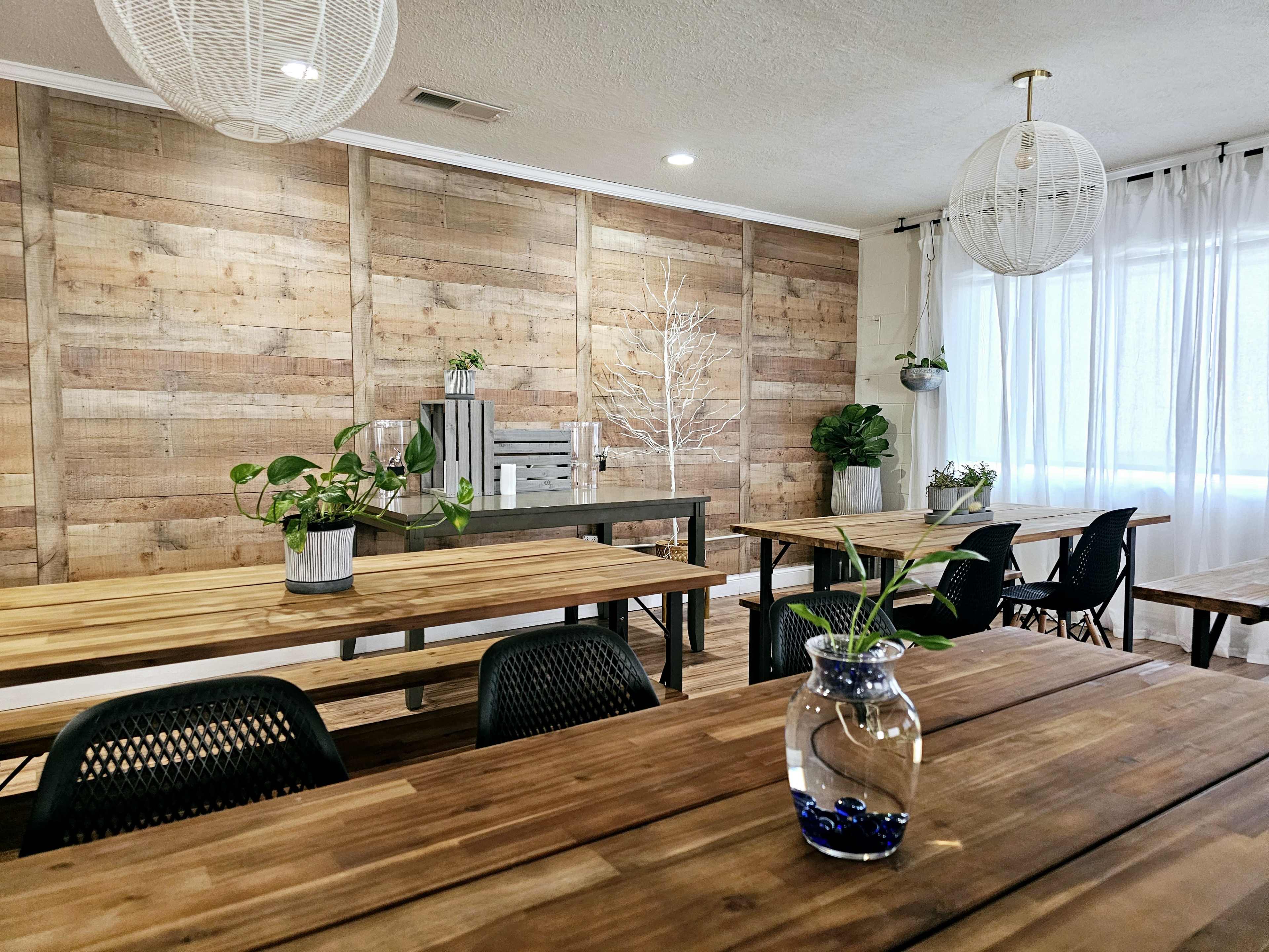 A bright, modern room with wooden tables, a large wooden accent wall, and potted plants on display.