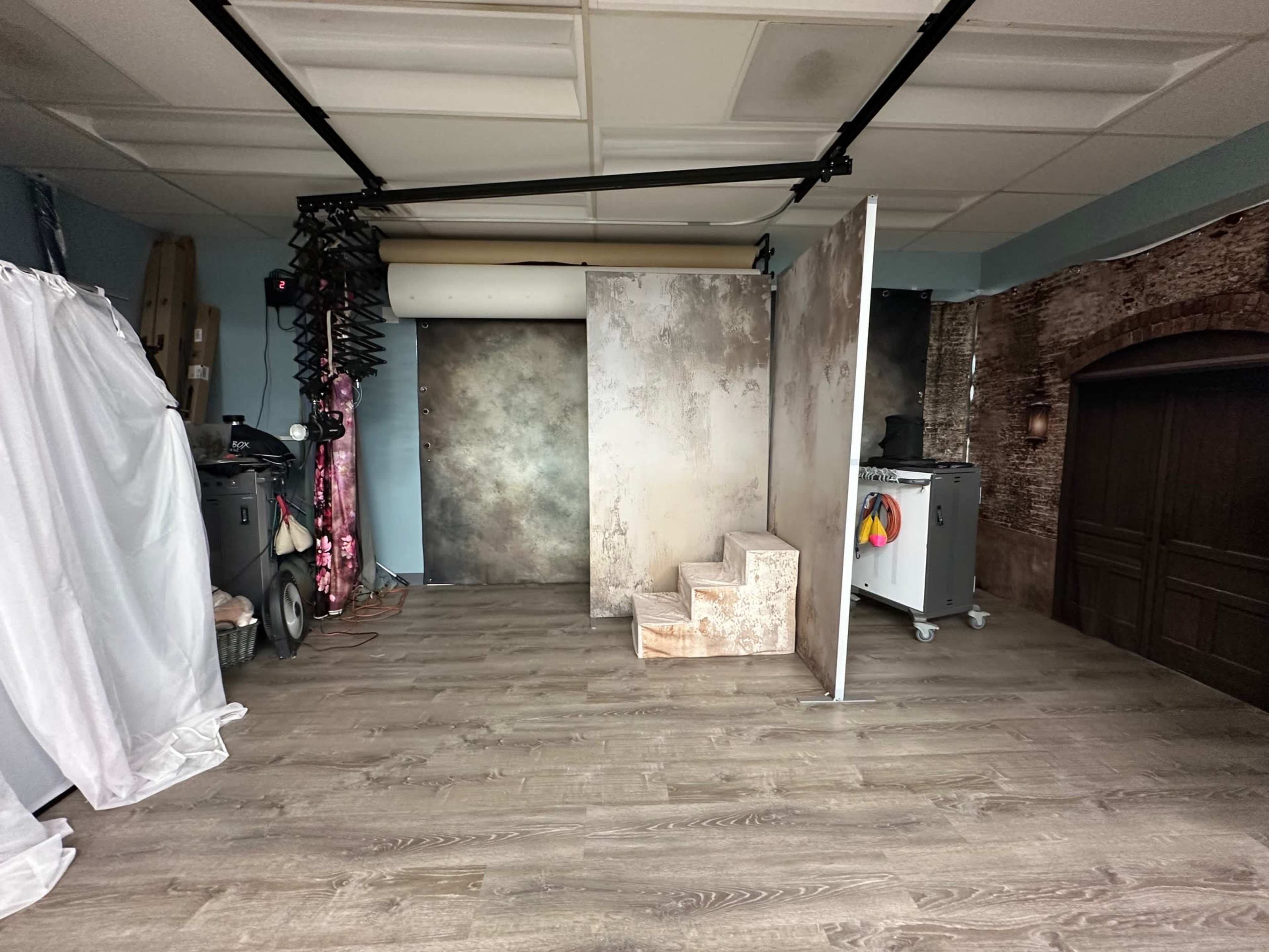 The image shows a photography studio with a wooden floor, backdrops, and a set of stairs leading up to a panel.
