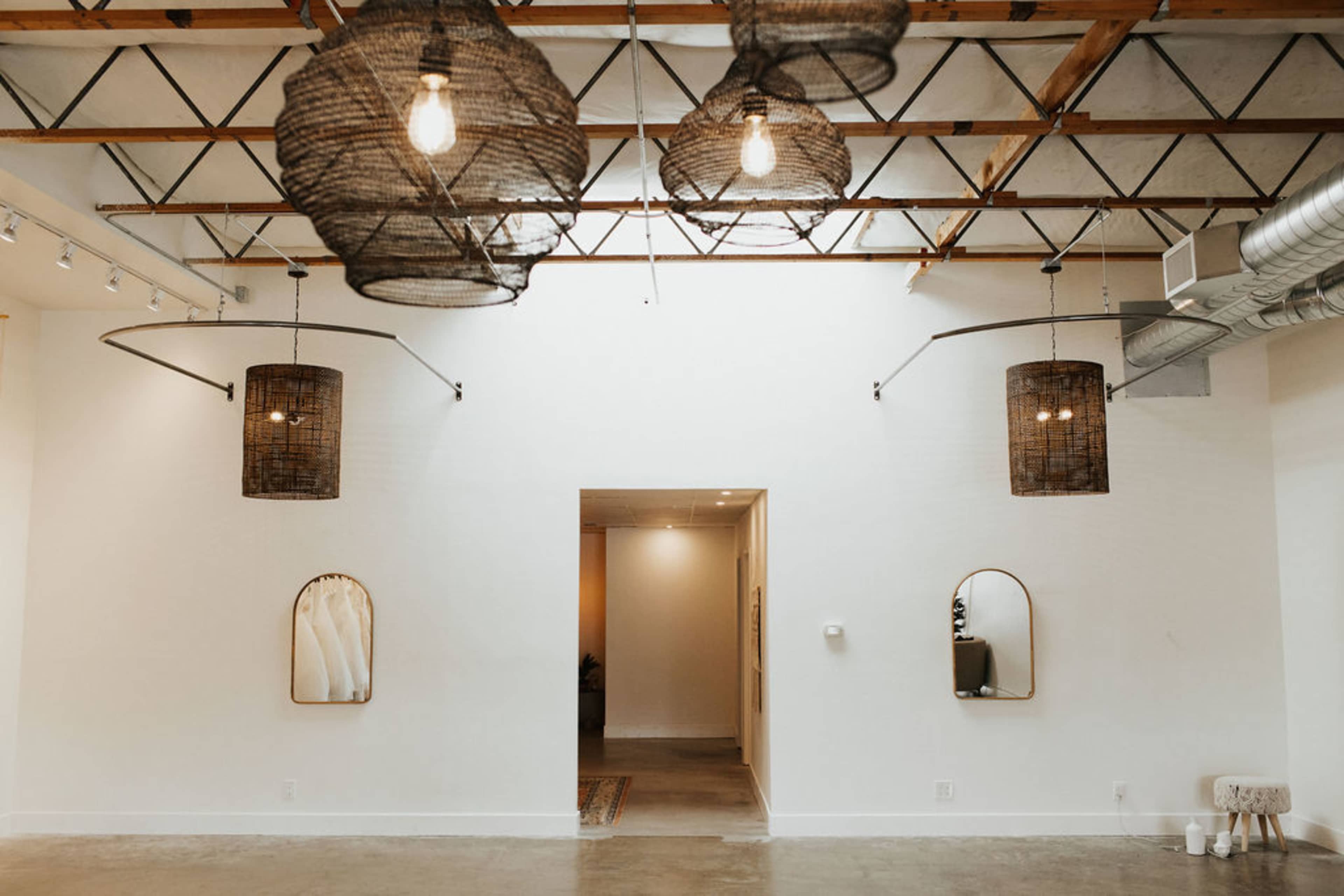 A modern interior space with a high ceiling, featuring three woven light fixtures, wall mirrors, and an entrance at the back.