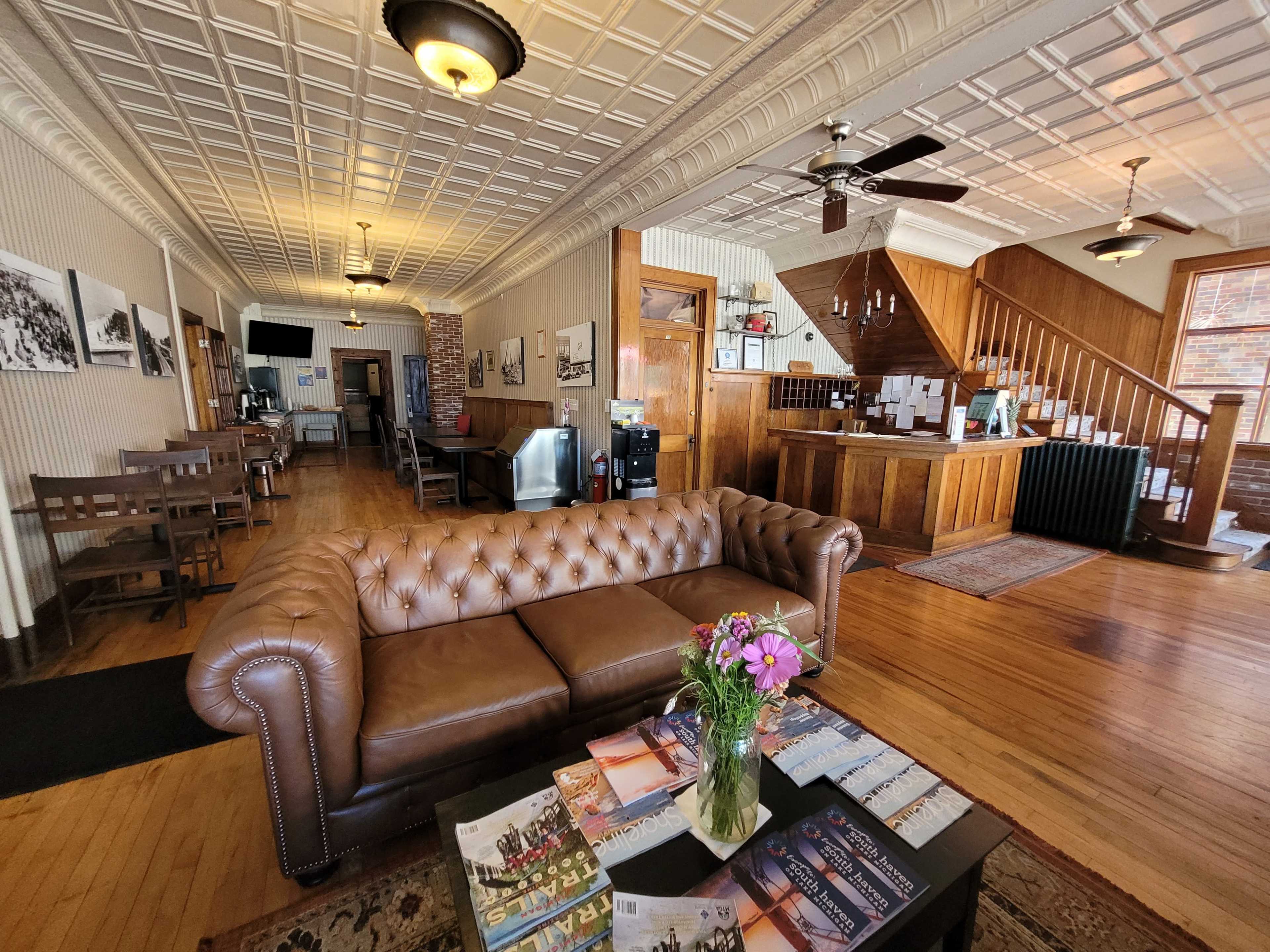 A cozy reception area with a brown leather sofa, a coffee station, and a staircase leading to an upper level.