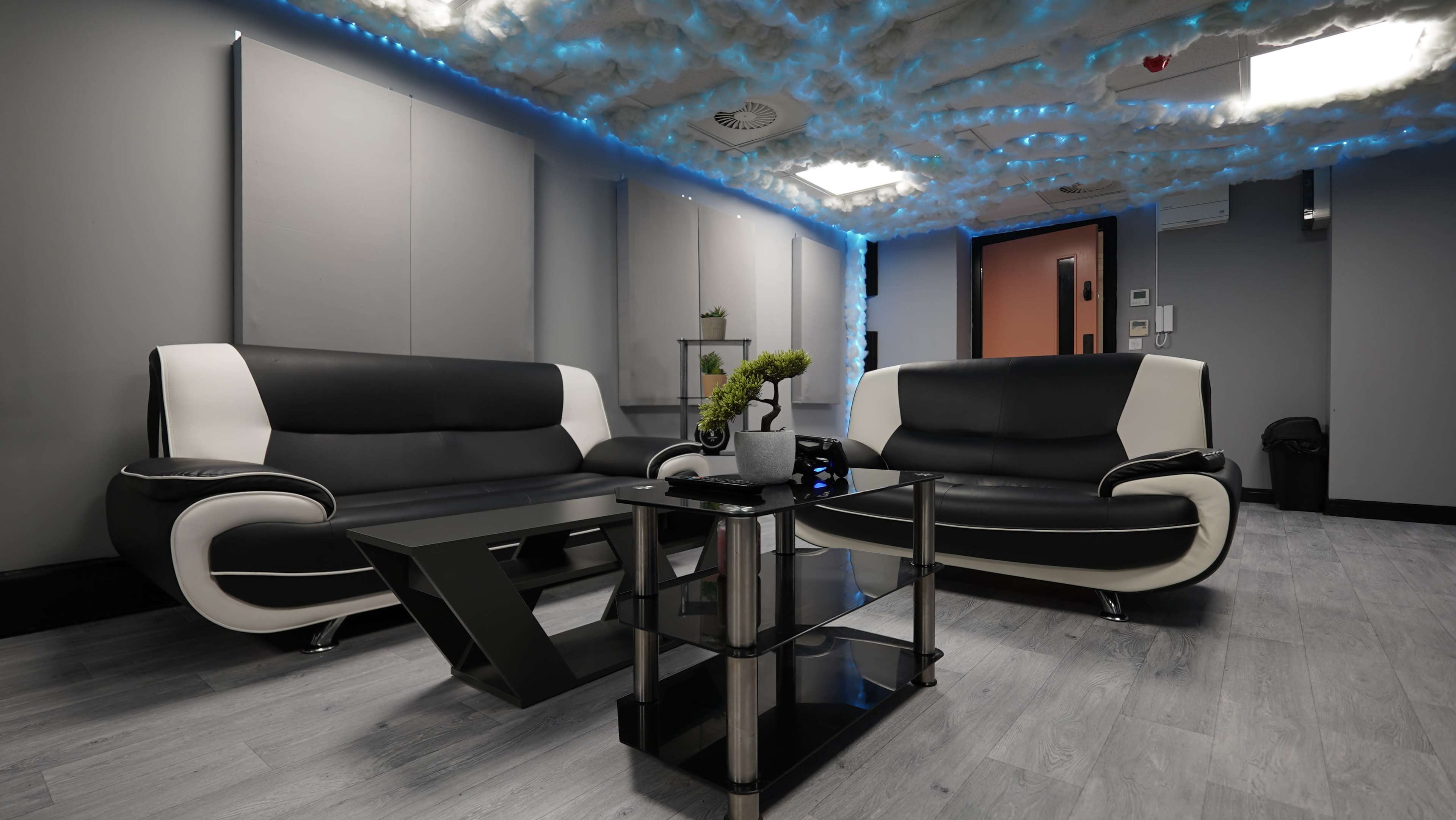 A modern seating area with two black and white sofas, a glass coffee table, and blue LED lights along the ceiling.