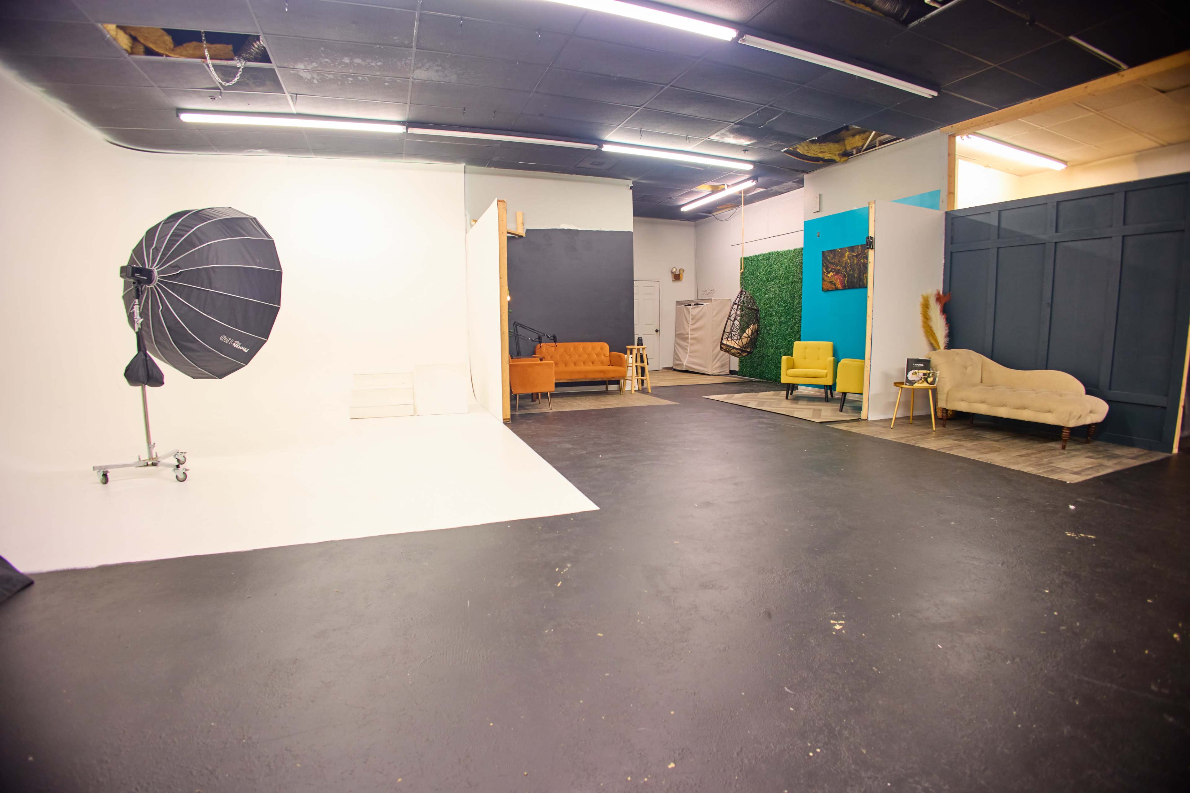 A photography studio with a white backdrop, lighting equipment, and various seating arrangements in different colors.