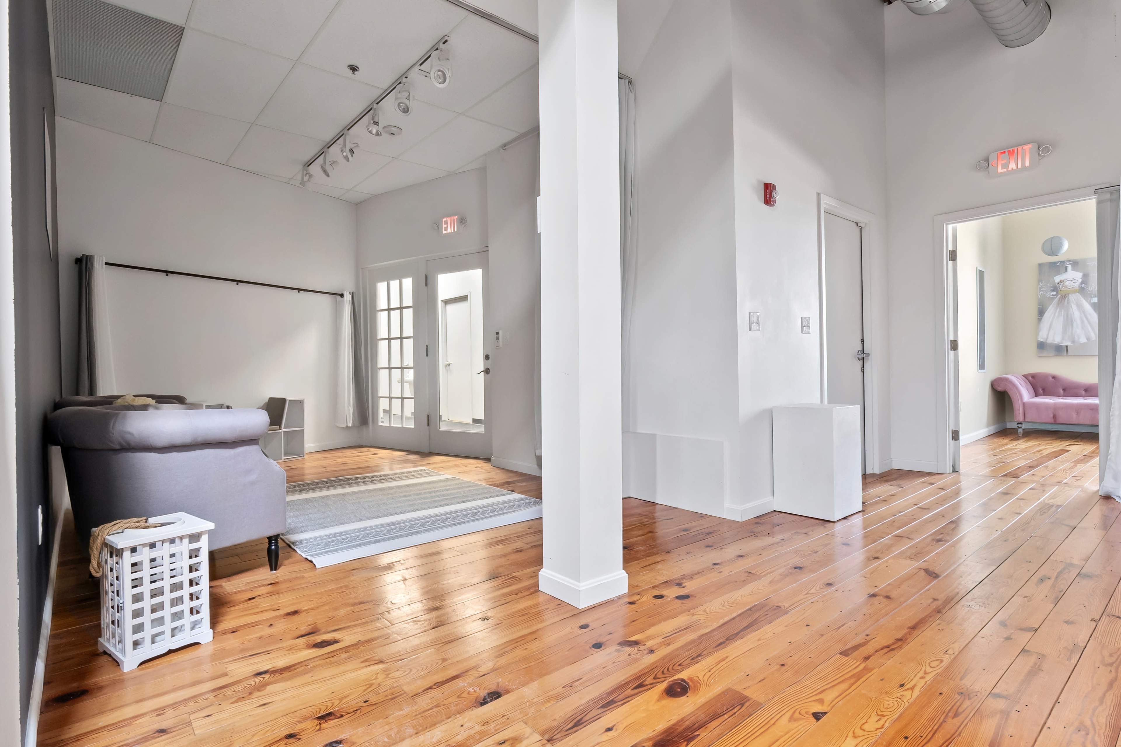 The image shows a bright, open interior space featuring wooden floors, white walls, and a modern seating area.