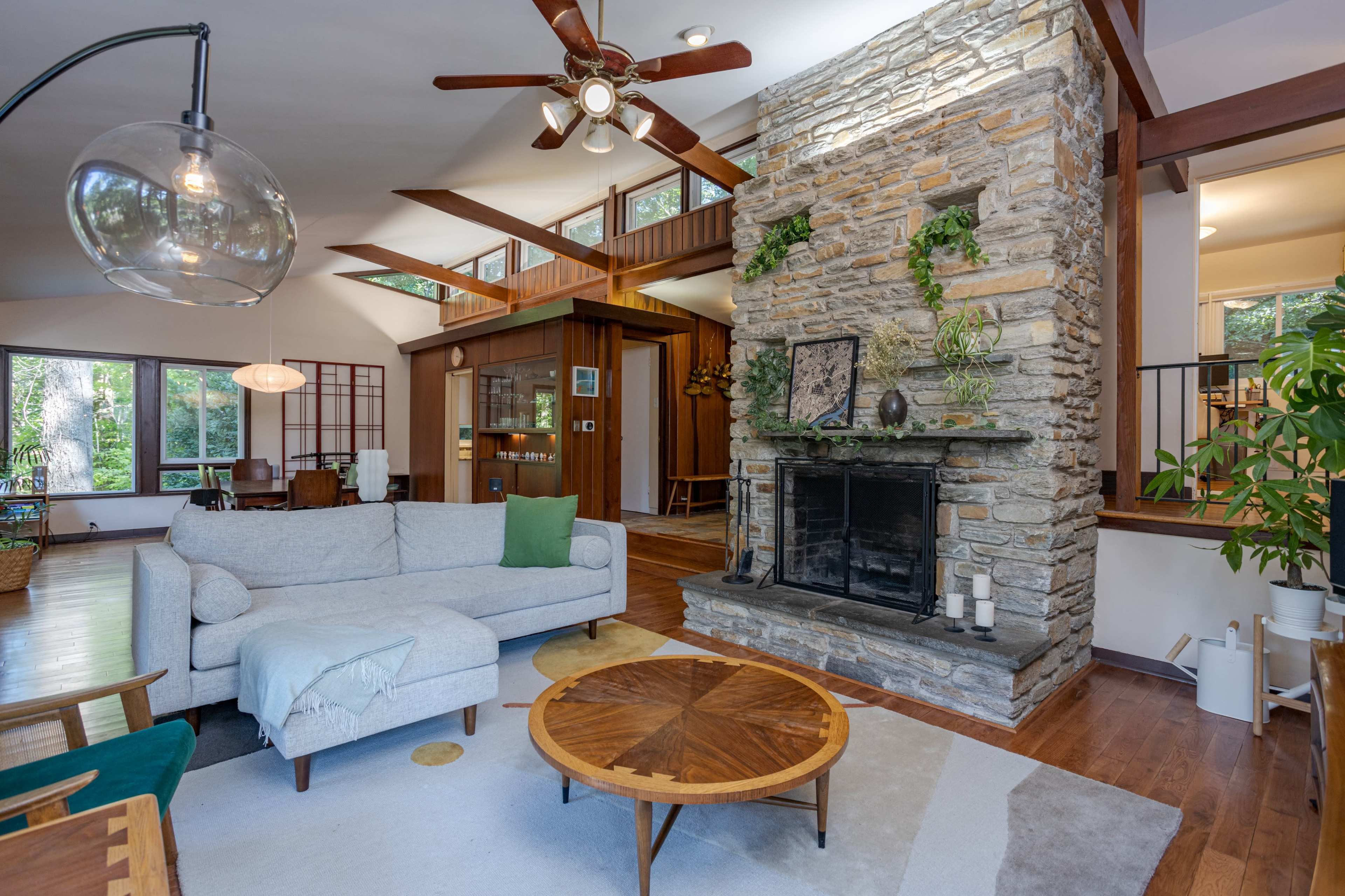 A cozy living room featuring a stone fireplace, wooden accents, and a light-colored sofa facing a round coffee table.