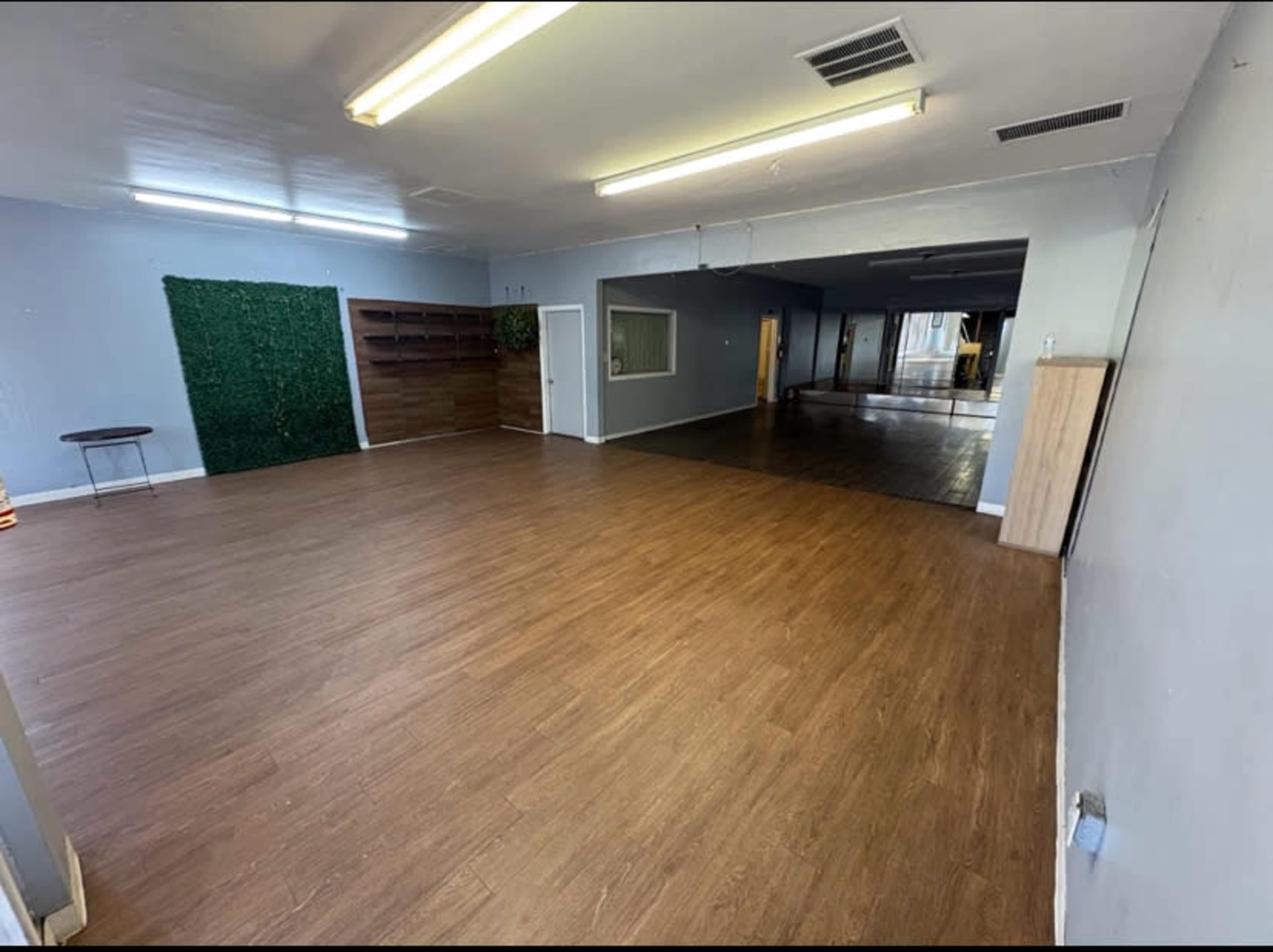 The image shows a spacious, empty interior with wooden flooring, a green wall feature on the left, and two adjoining areas visible through an open doorway.
