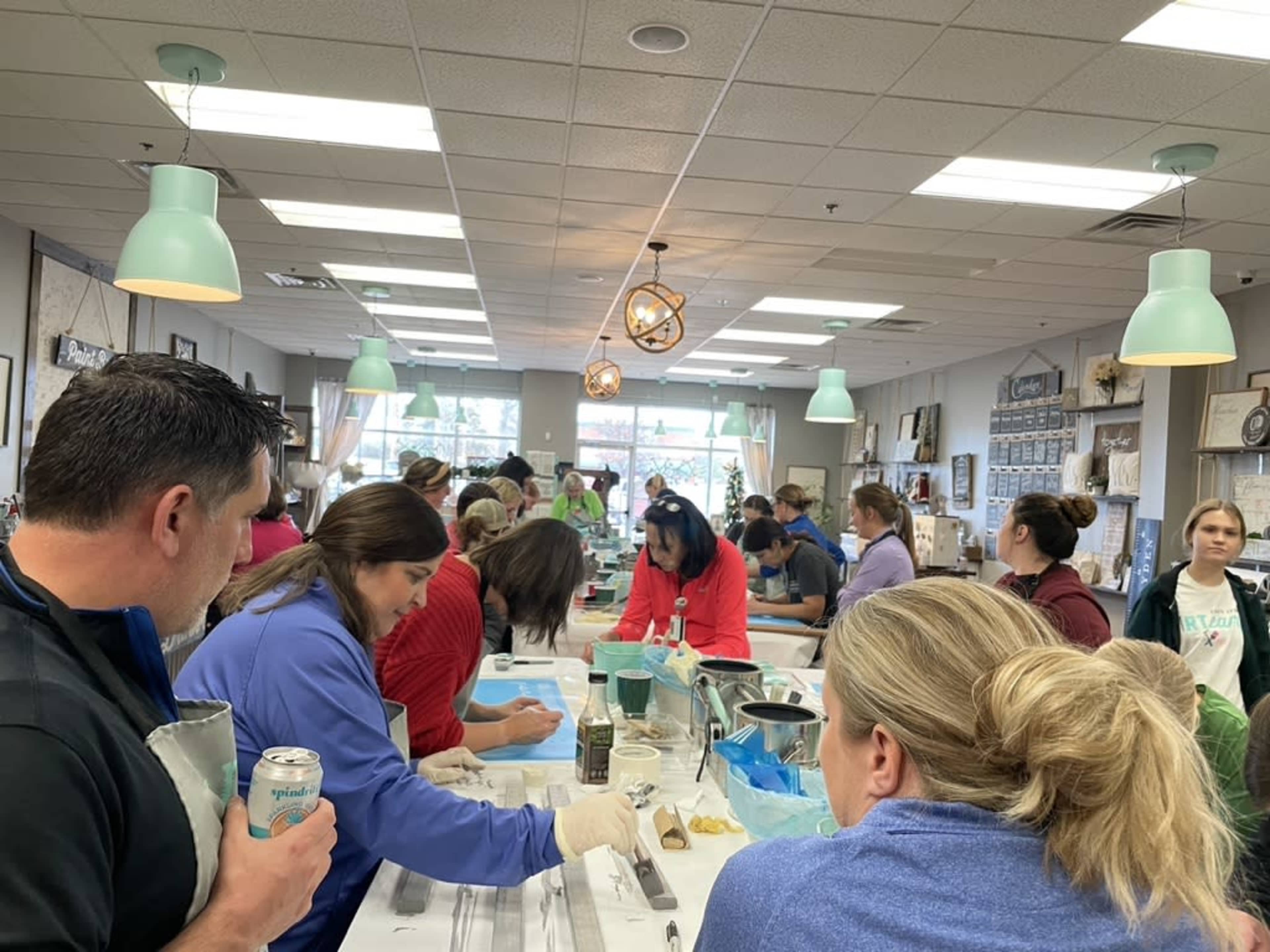 A group of people are gathered around tables in a bright, spacious room, engaged in a hands-on activity with various materials and equipment.