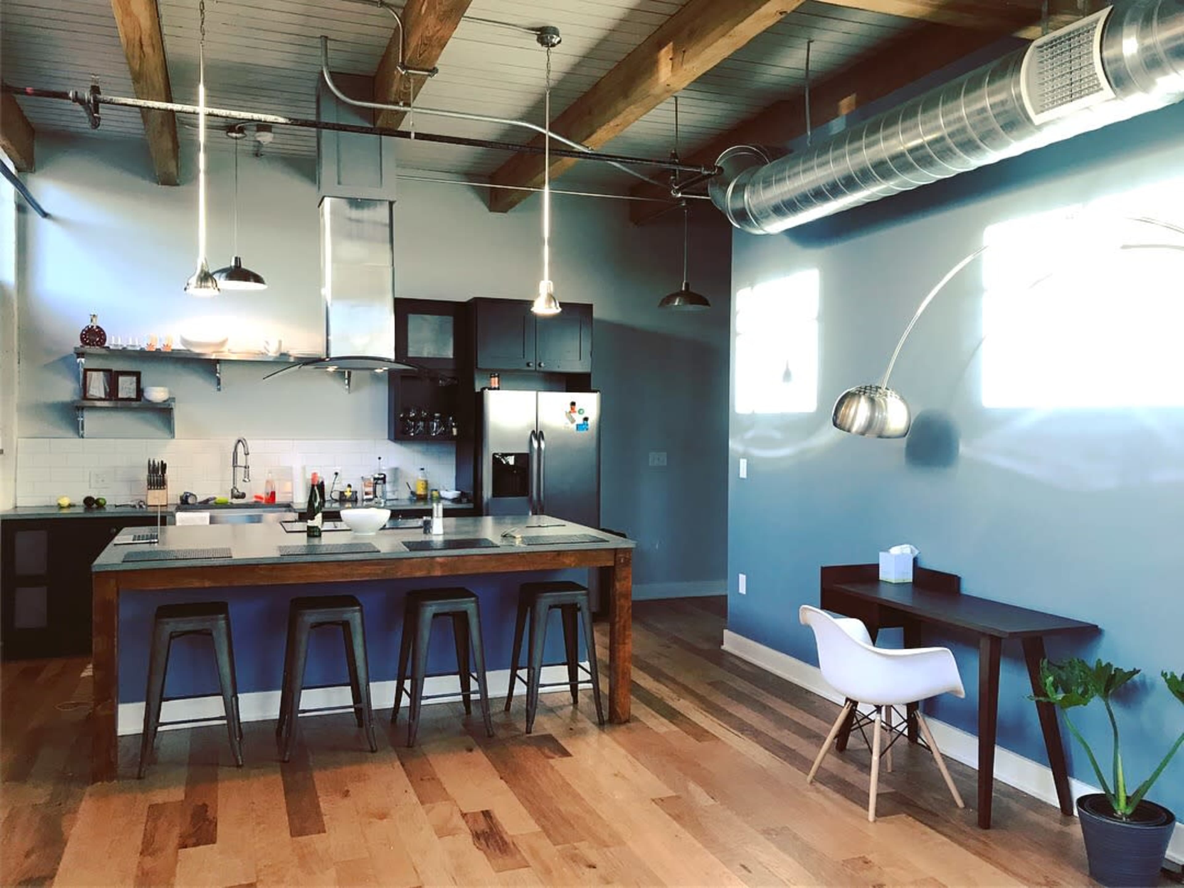 A modern kitchen with a large island, wooden floors, and industrial-style lighting.