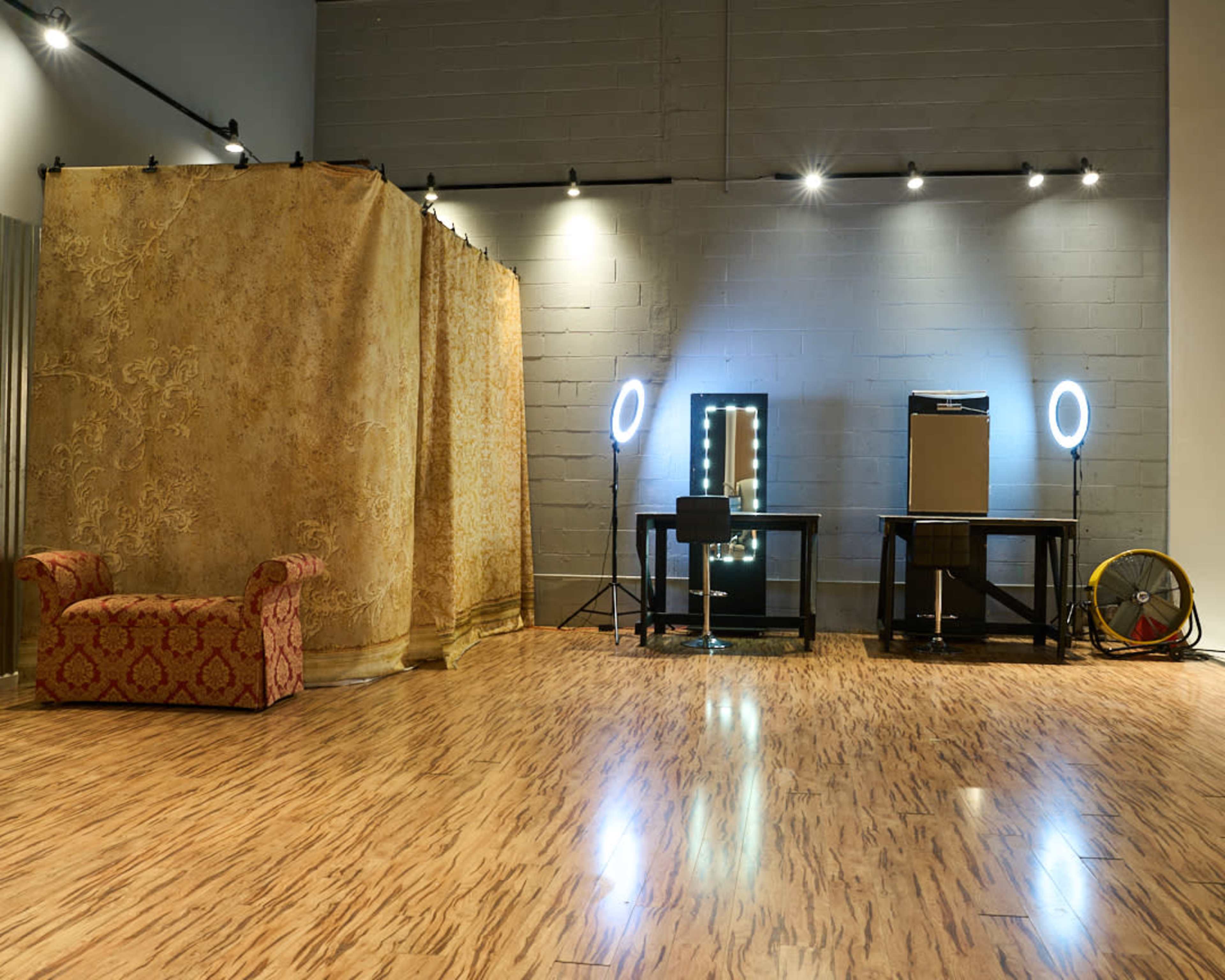 The image shows a spacious room with a patterned fabric partition, two lighted mirrors, and a table with audio equipment.
