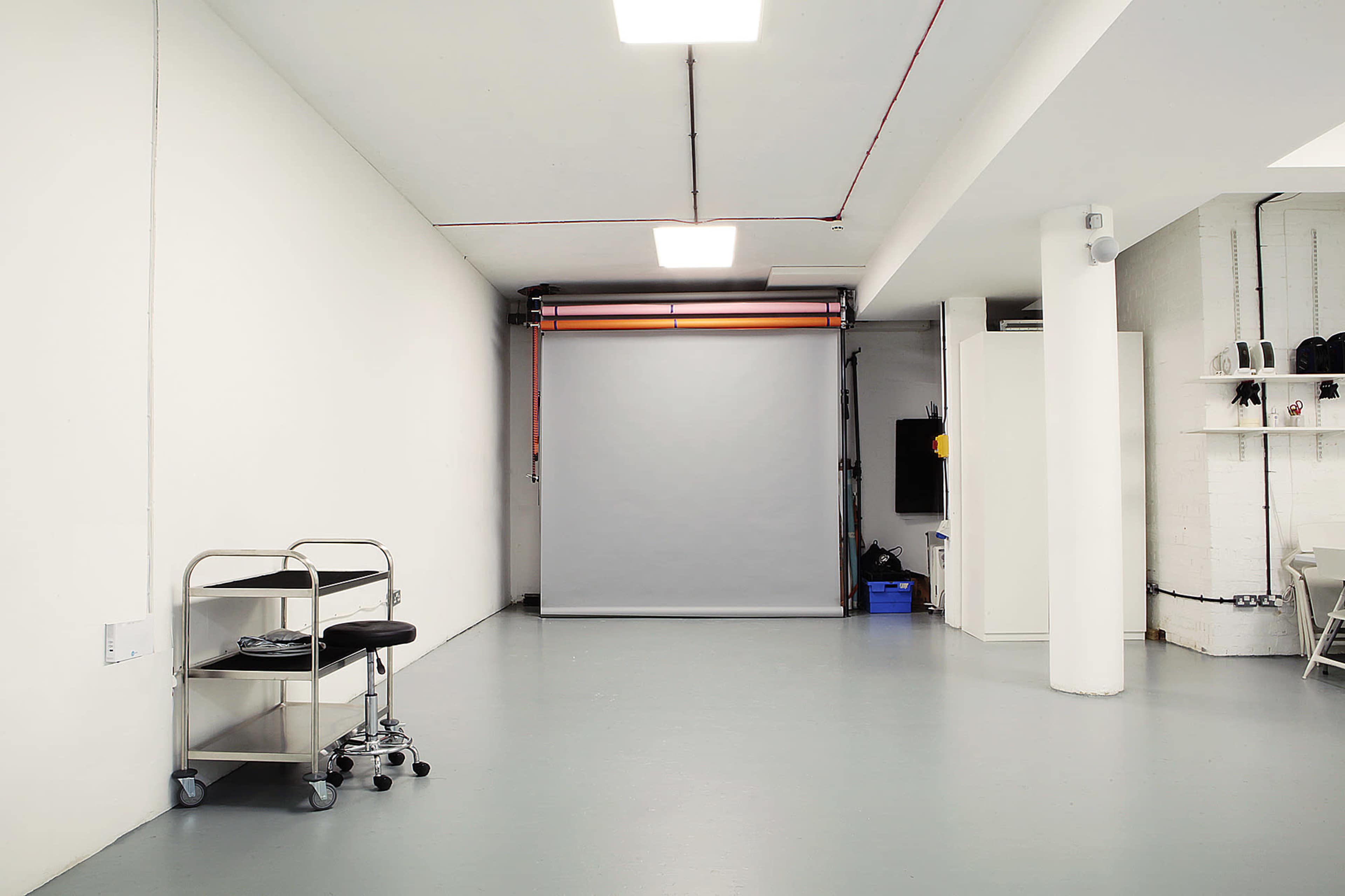 A minimalist studio space with a gray backdrop, a wheeled cart, and an empty floor.