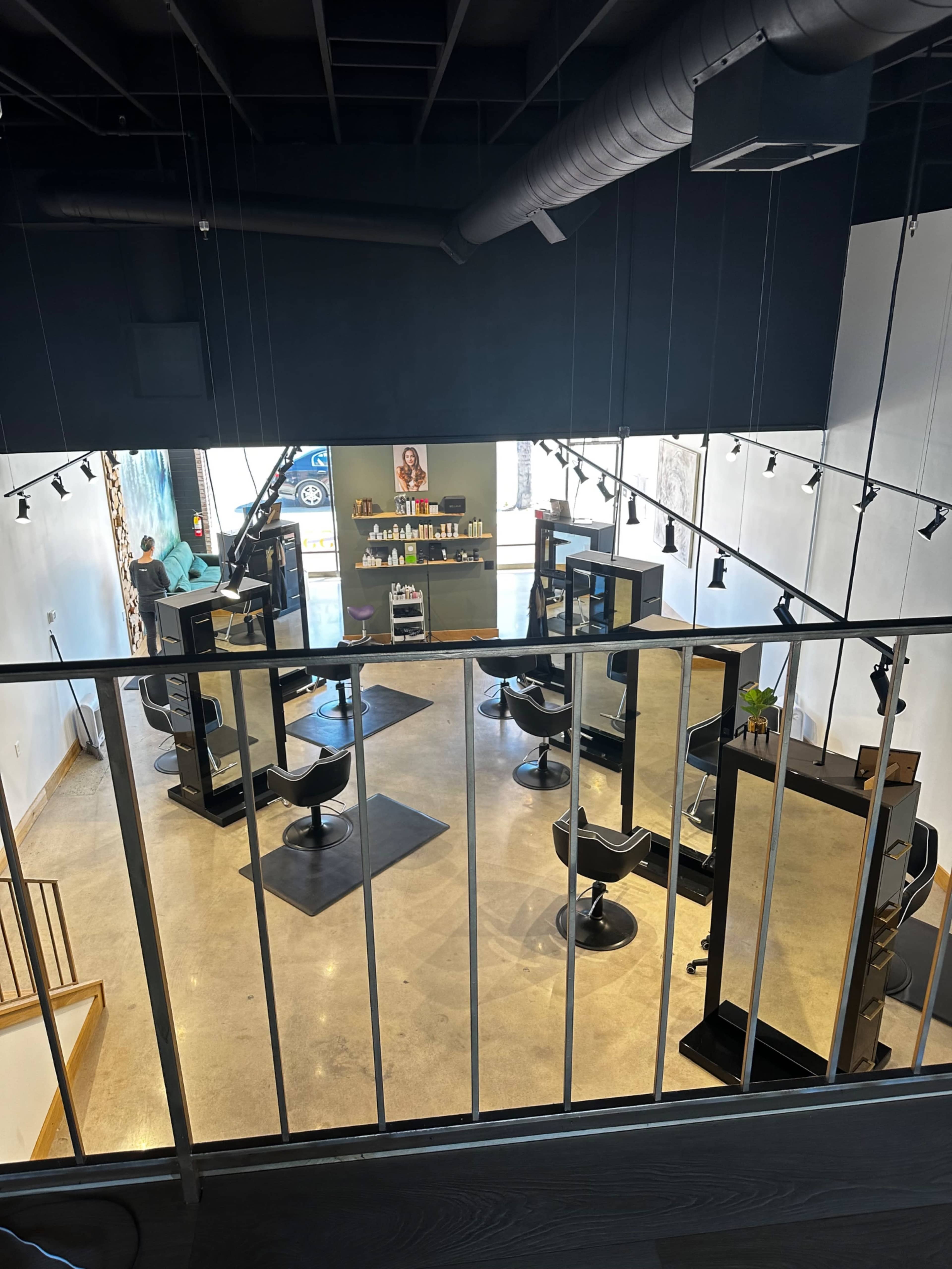 A brightly lit hair salon with several styling stations, mirrors, and a staircase in the foreground.
