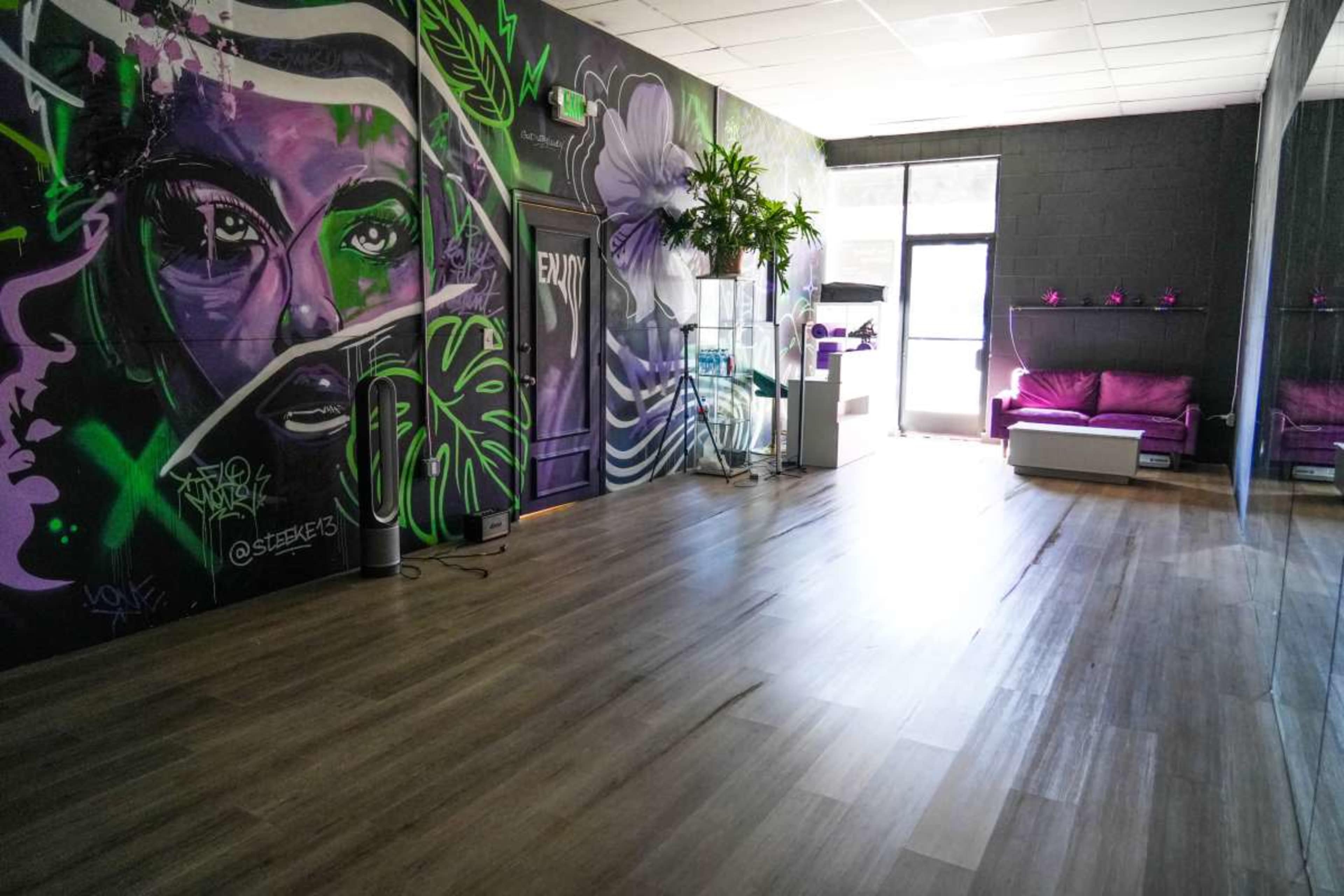 The image shows a brightly lit interior space featuring a mural with vibrant graffiti art on one wall and minimalist furniture arranged on a wooden floor.
