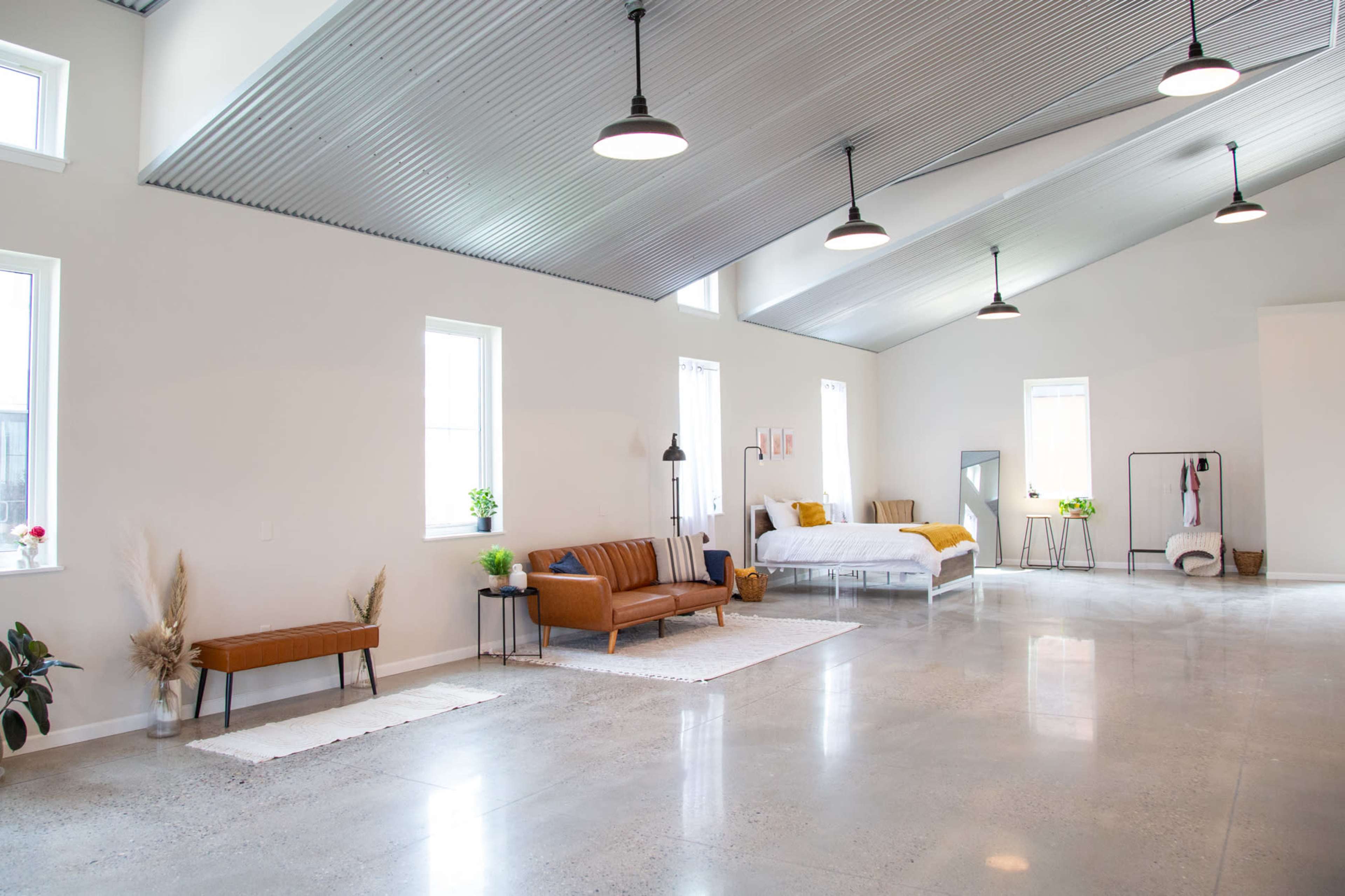 A spacious, modern interior with a sofa, bed, and minimal decor, featuring large windows and polished concrete floors.