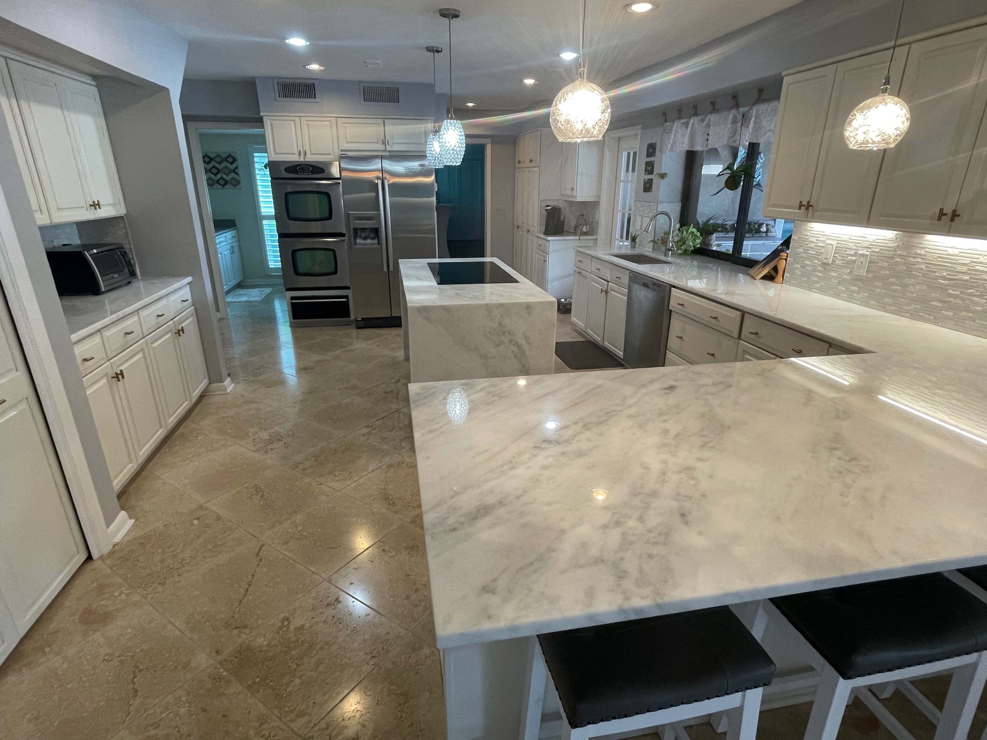 A modern kitchen featuring white cabinetry, marble countertops, and stainless steel appliances.