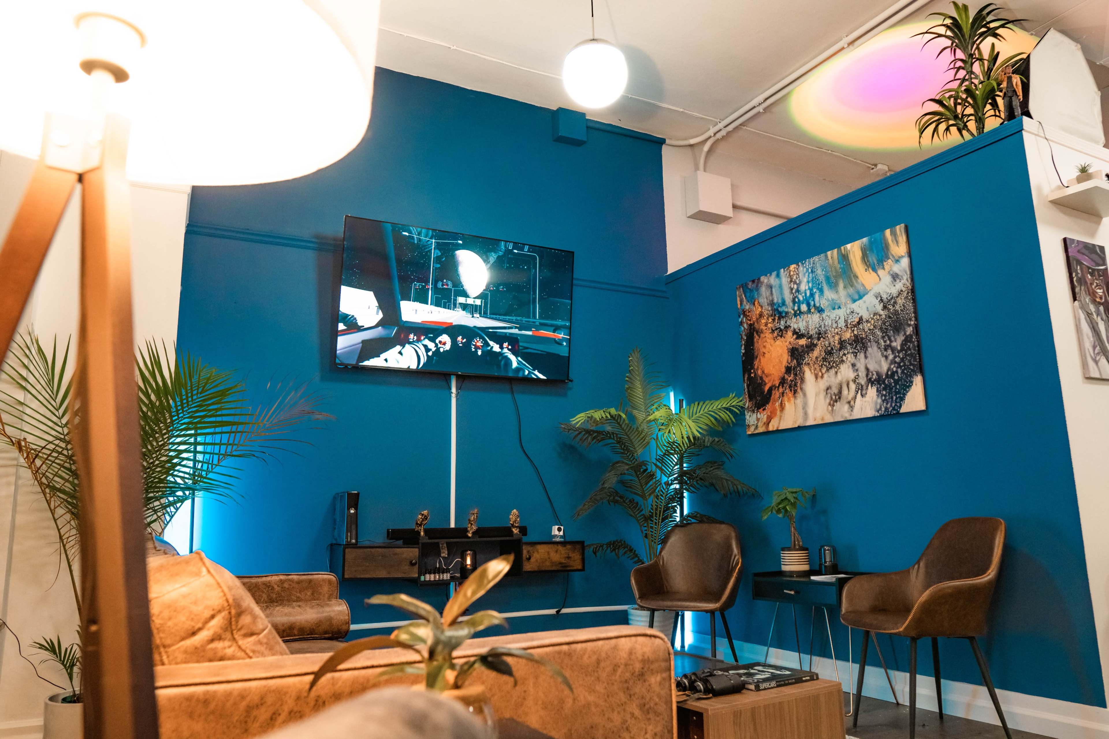 A cozy lounge area features a blue wall, a television displaying a race scene, and modern furniture including two chairs and a coffee table.