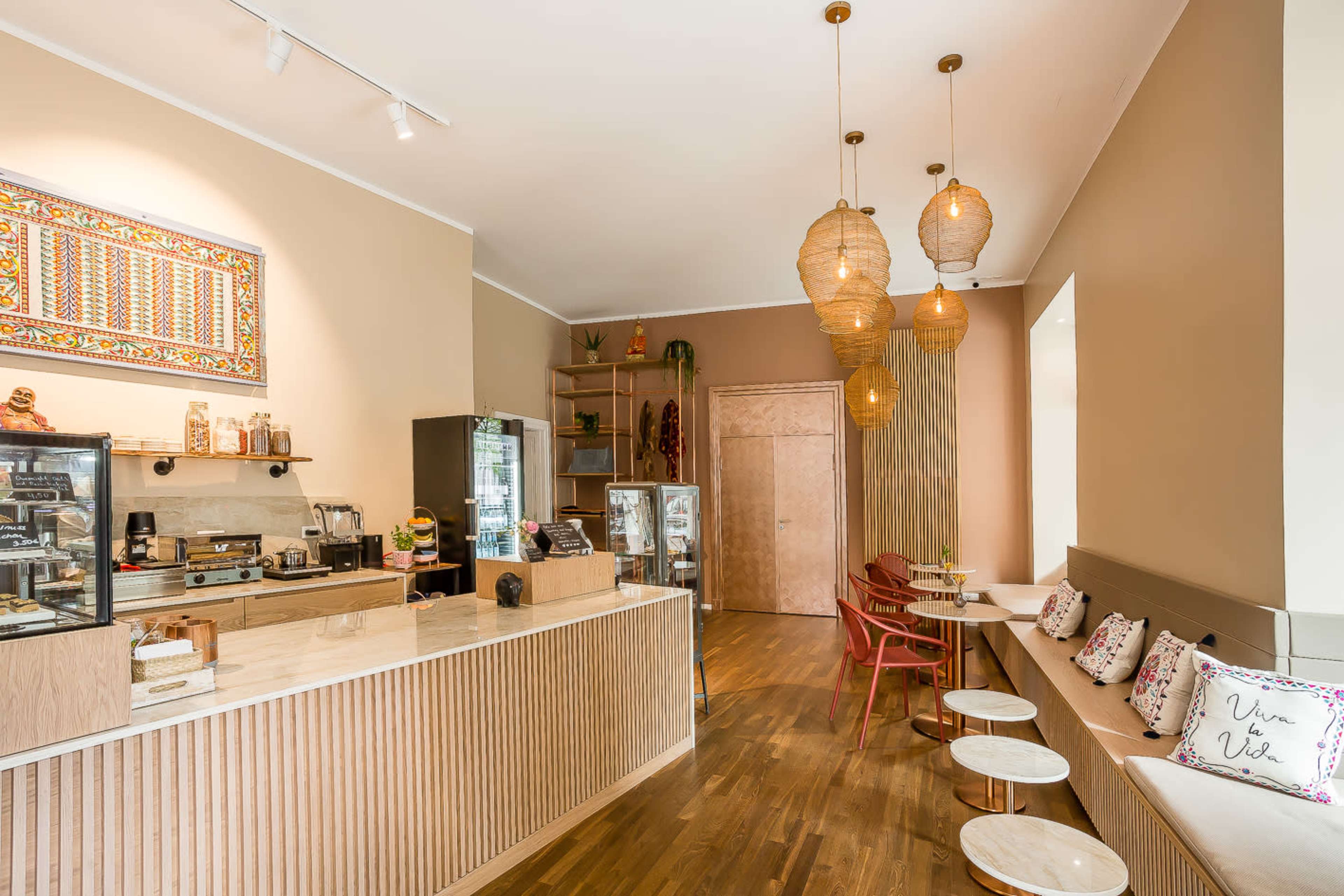 A modern café interior with wooden flooring, a counter displaying food and drinks, and pendant lighting.
