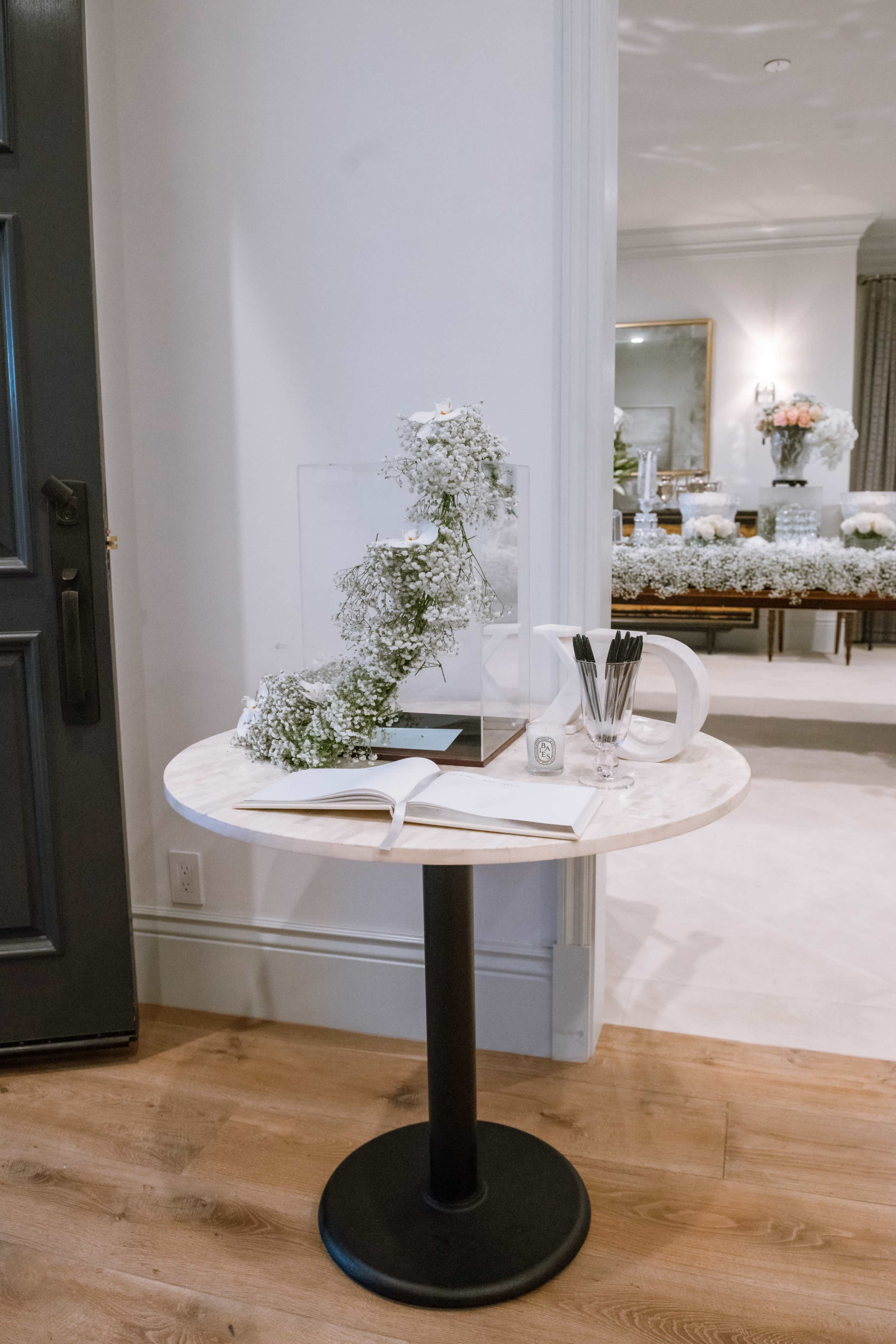 A round marble table with a glass display featuring flowers and an open book sits near a door in a well-lit interior space.
