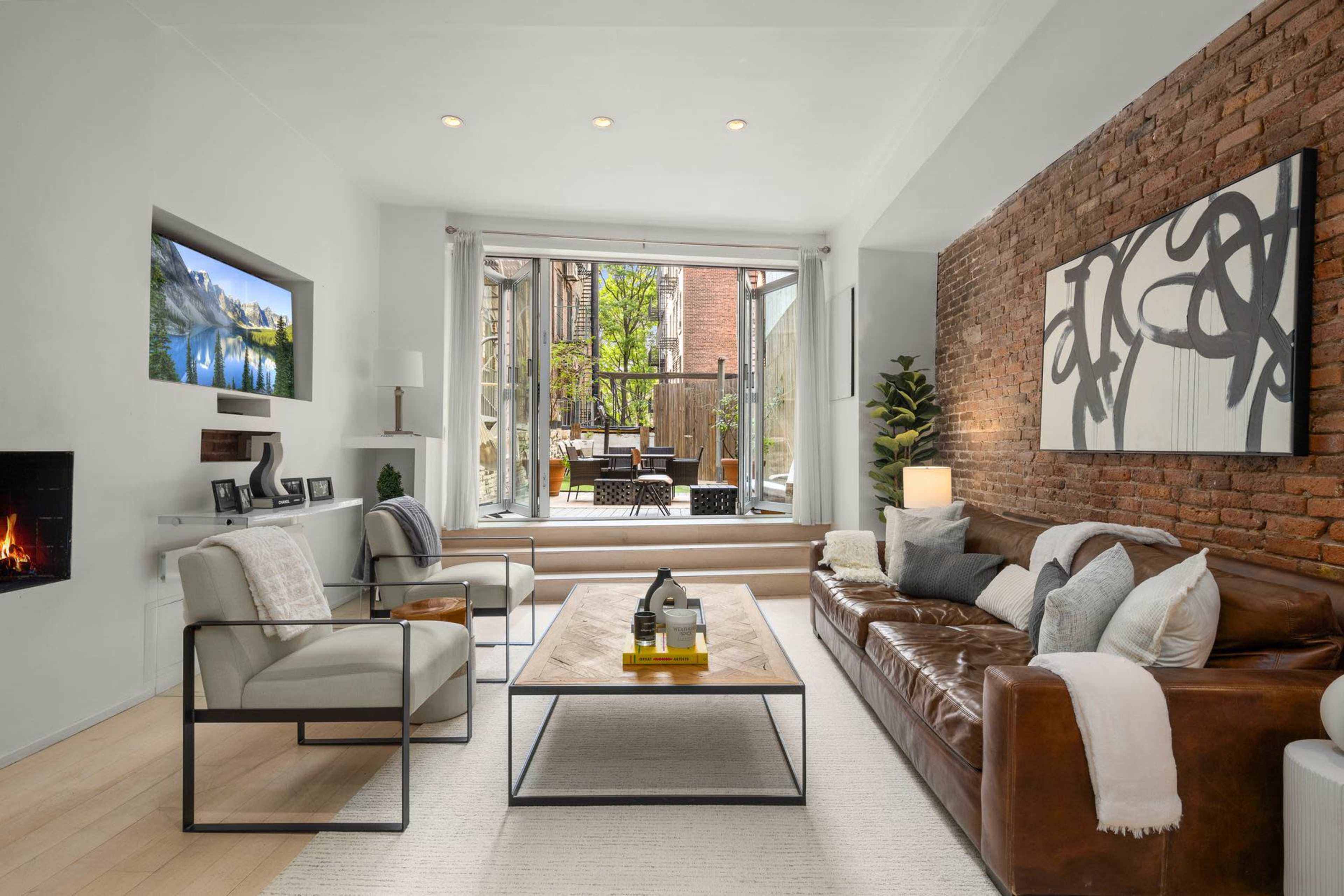 A modern living room with a leather sofa, two chairs, a coffee table, and large windows opening to a patio area.