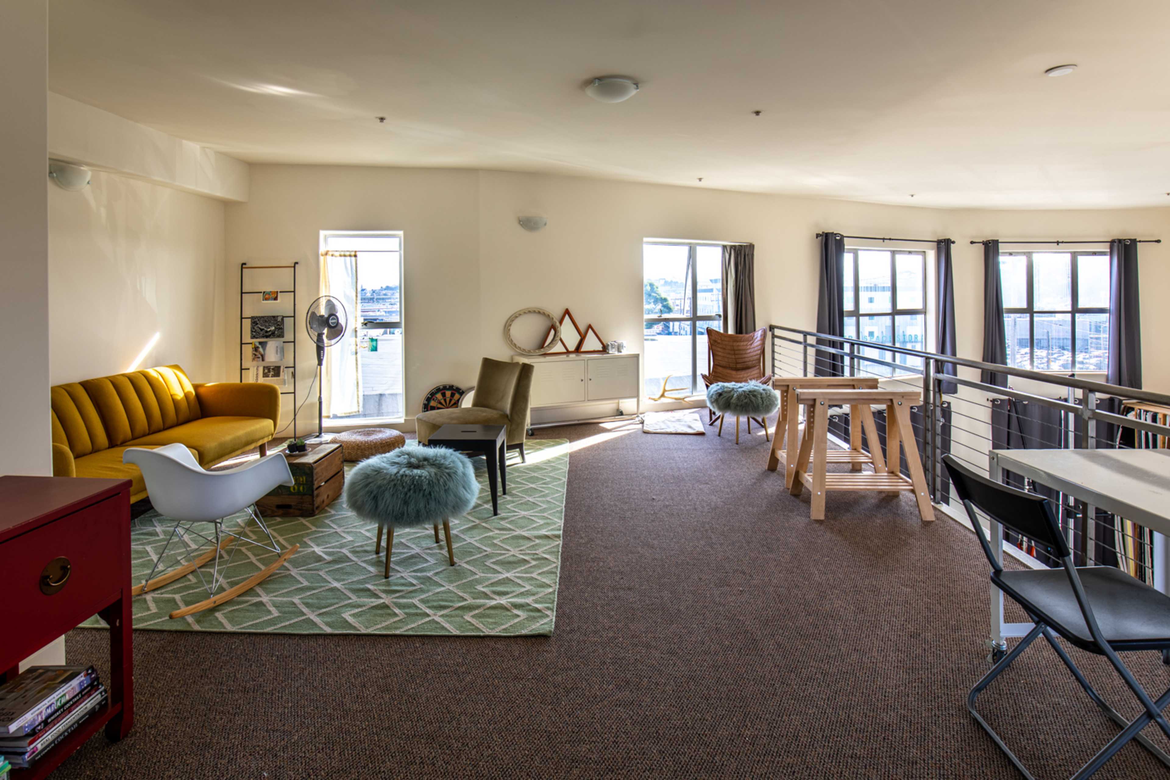 A spacious, modern loft-style living area with a yellow sofa, an armchair, a coffee table, and large windows allowing natural light to flow in.