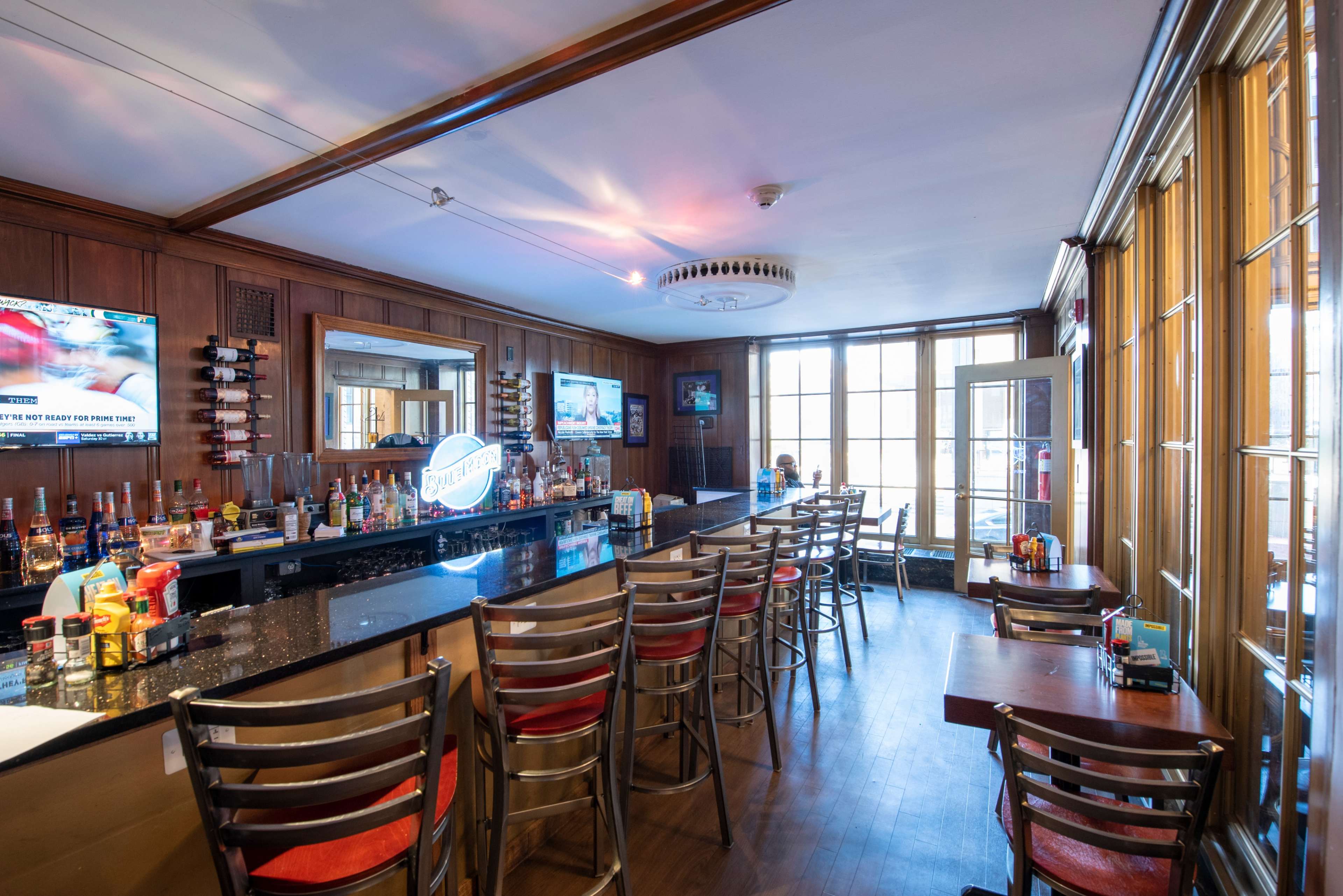 A bar area with wooden paneling, a granite countertop, several bar stools, and televisions mounted on the walls.