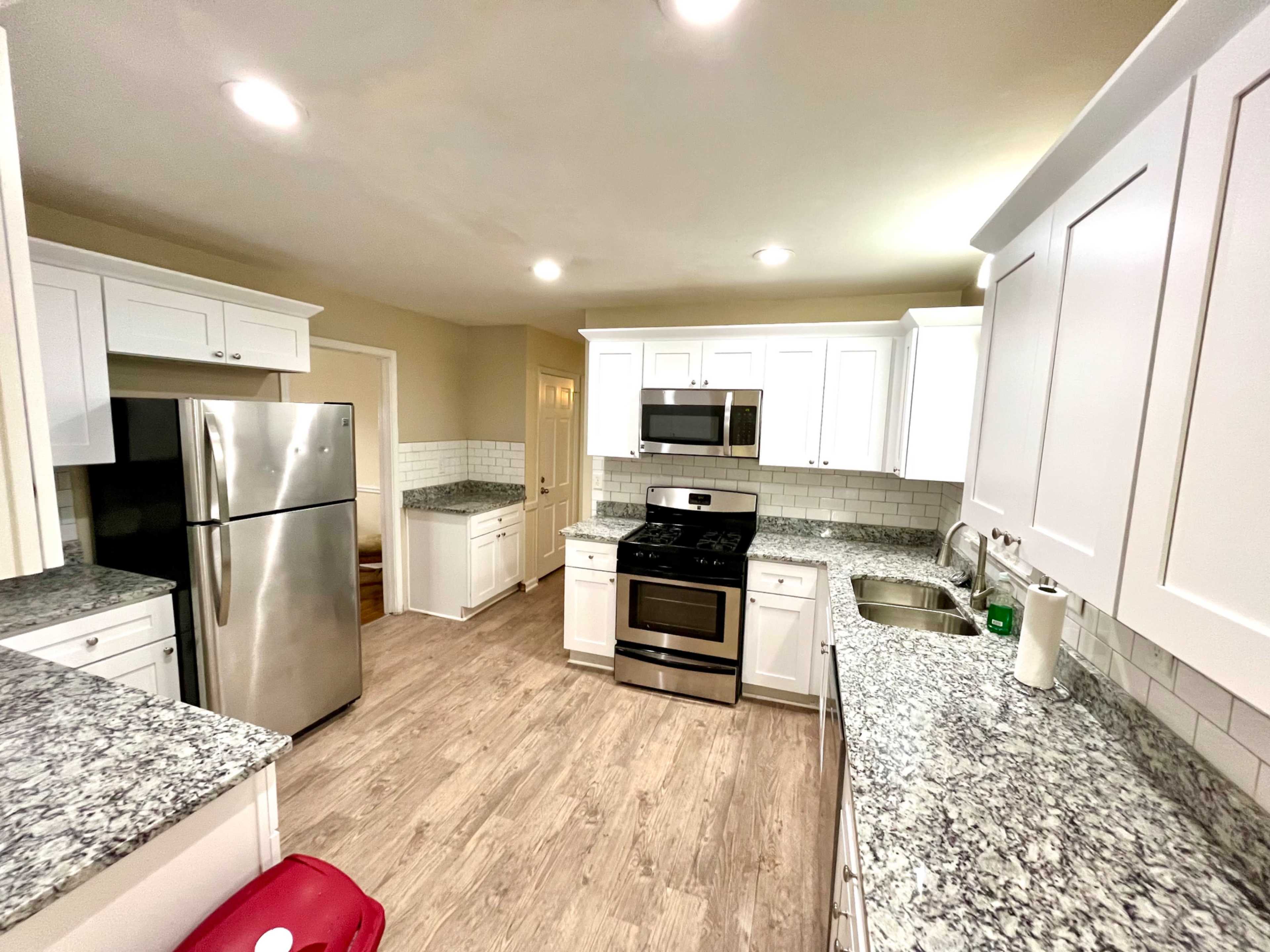 The image shows a modern kitchen with white cabinetry, stainless steel appliances, and granite countertops.