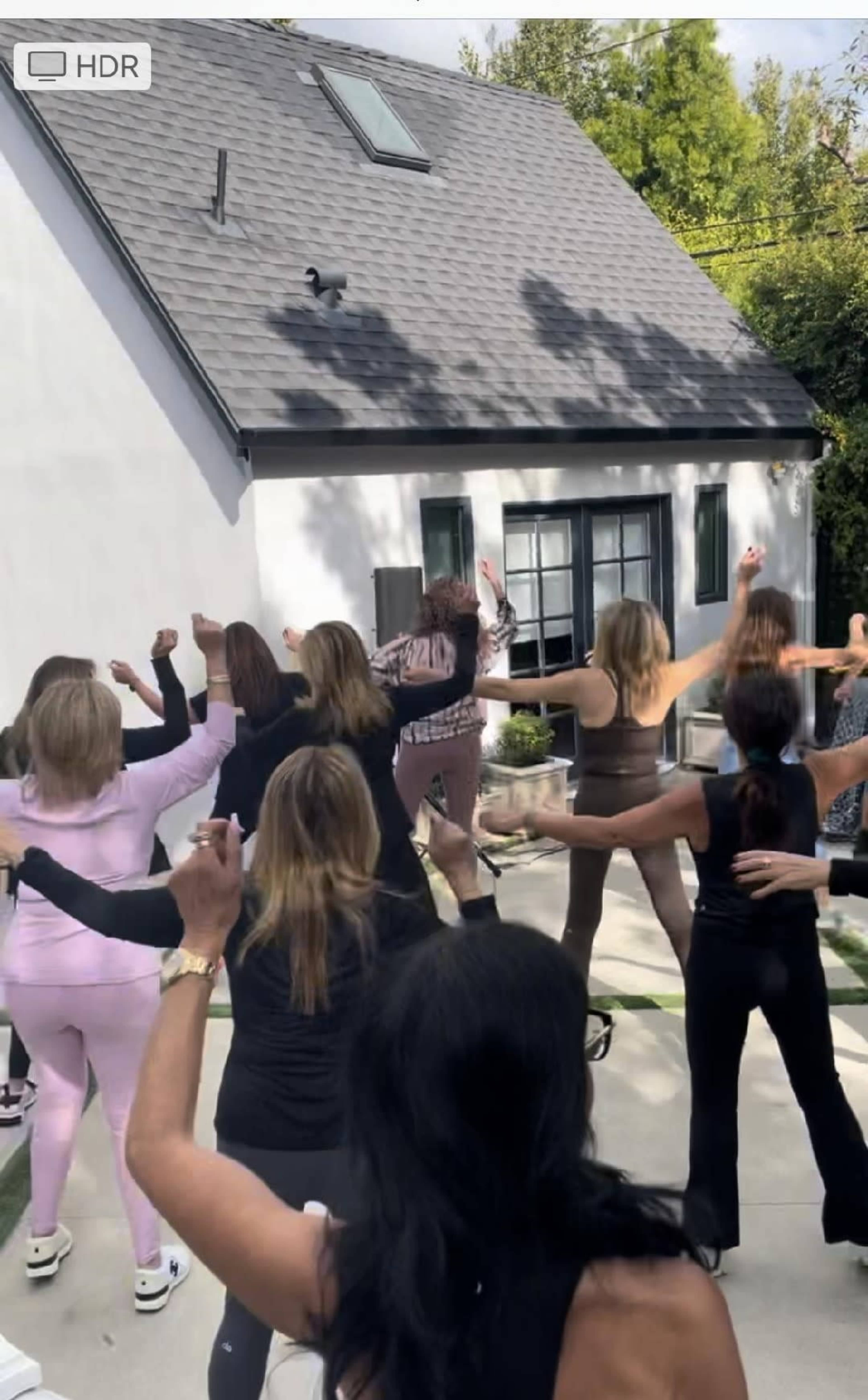 A group of women are dancing outdoors in a backyard area near a house.