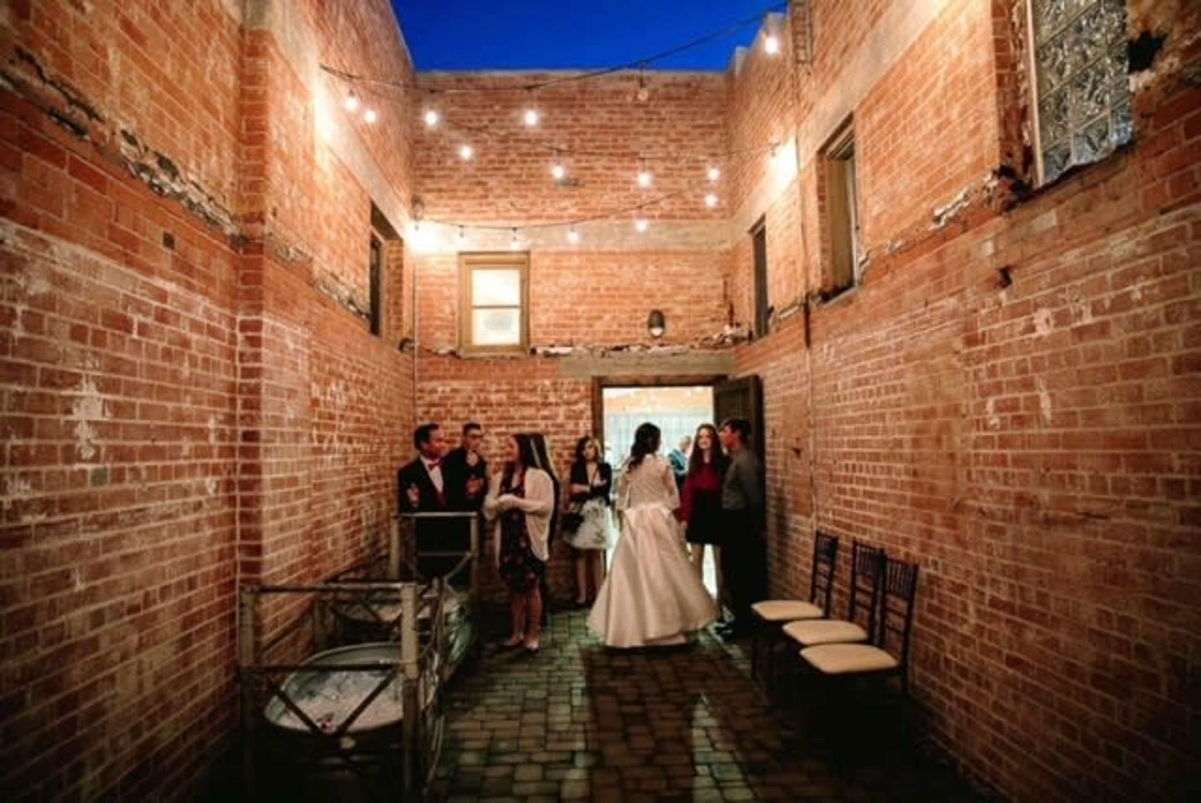 A group of people gathers in a brick-walled interior space with string lights illuminating the setting.