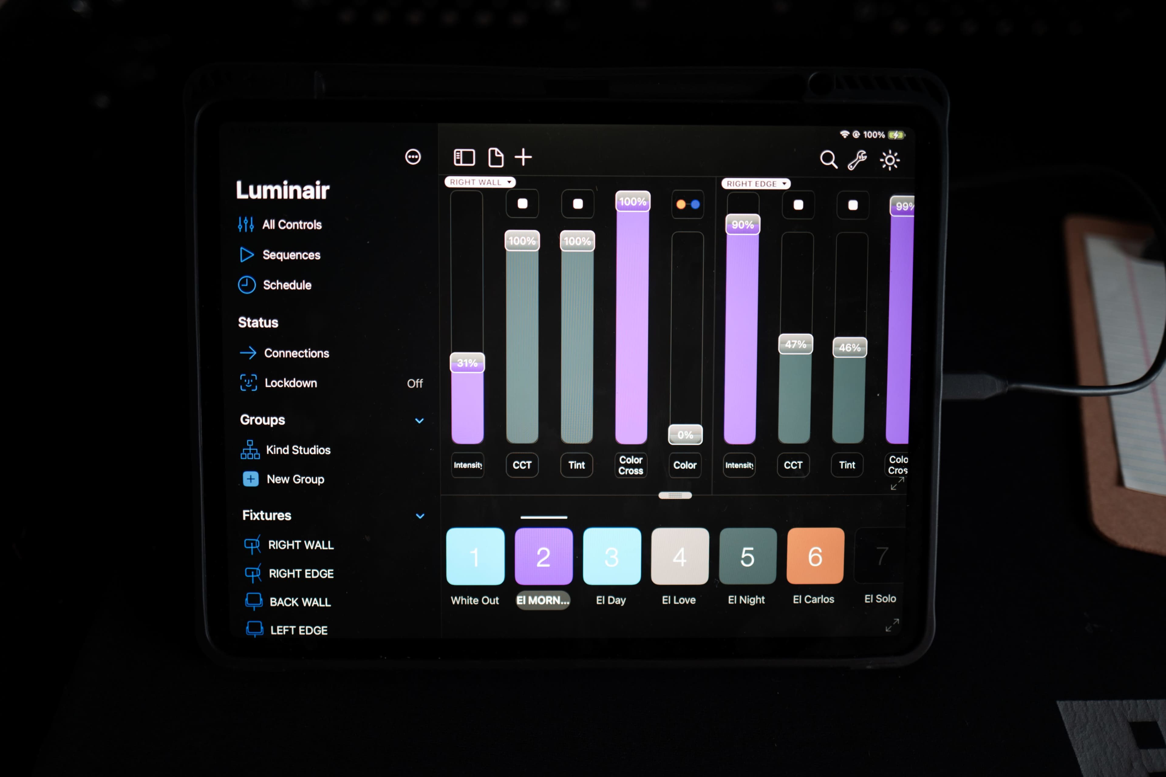 A digital tablet displays a lighting control application with various sliders and color options for managing lighting fixtures.