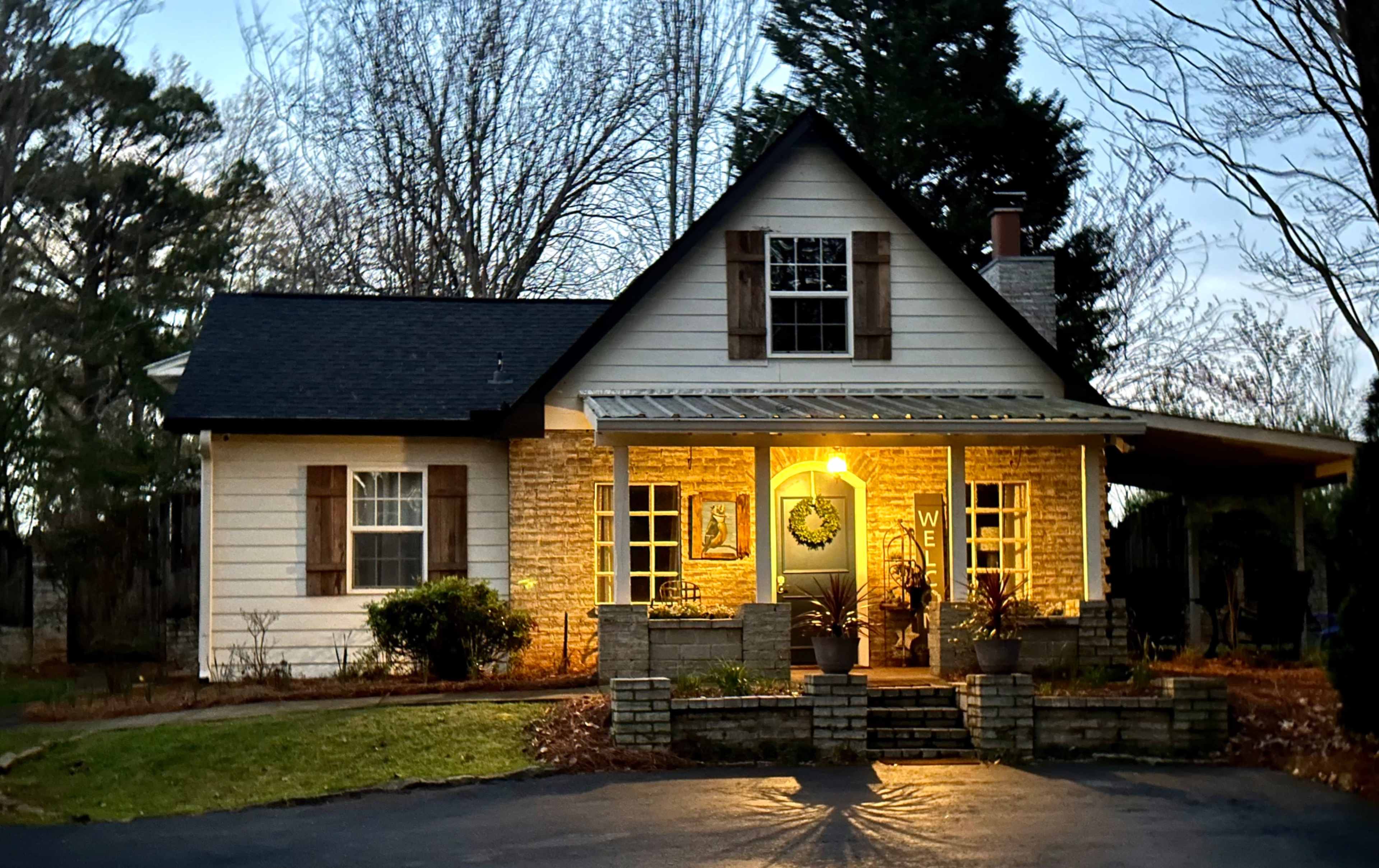 A single-story house features a porch with a welcoming wreath and landscaped front yard, illuminated by warm light in the evening.