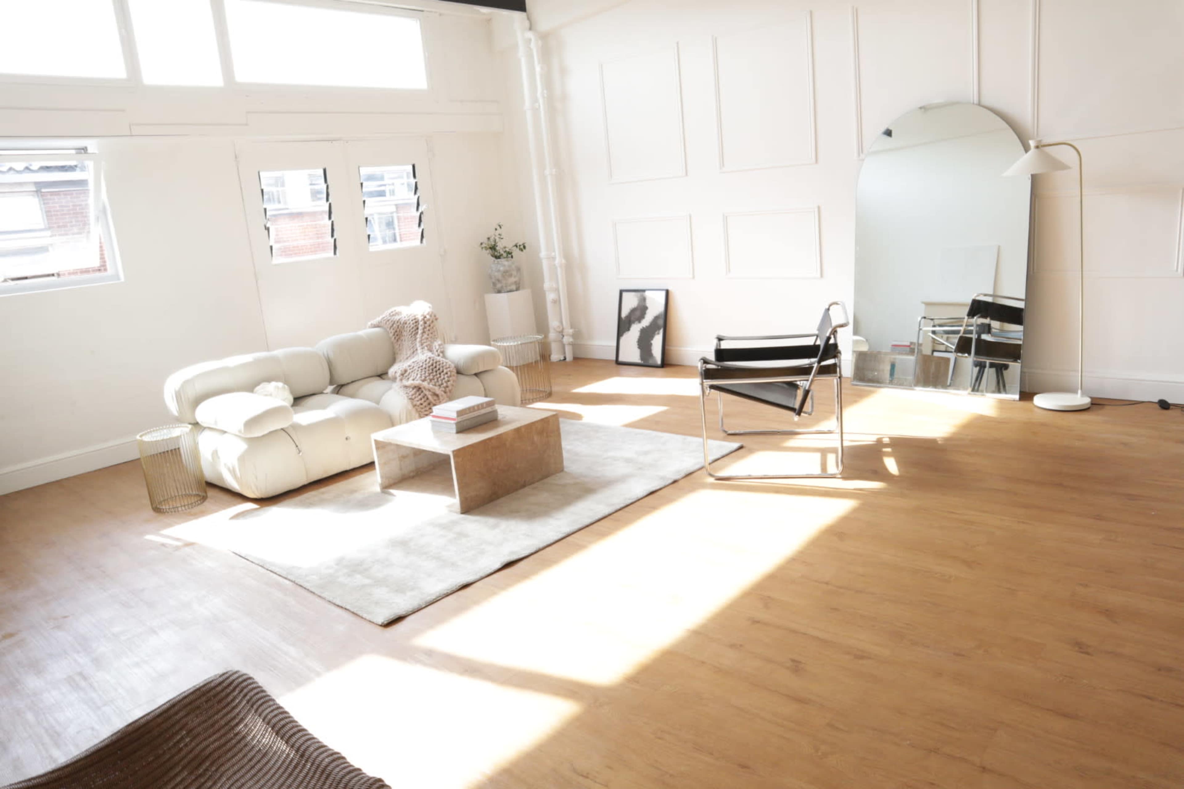 A bright, modern living room with a white sofa, a coffee table, and large windows allowing natural light to fill the space.