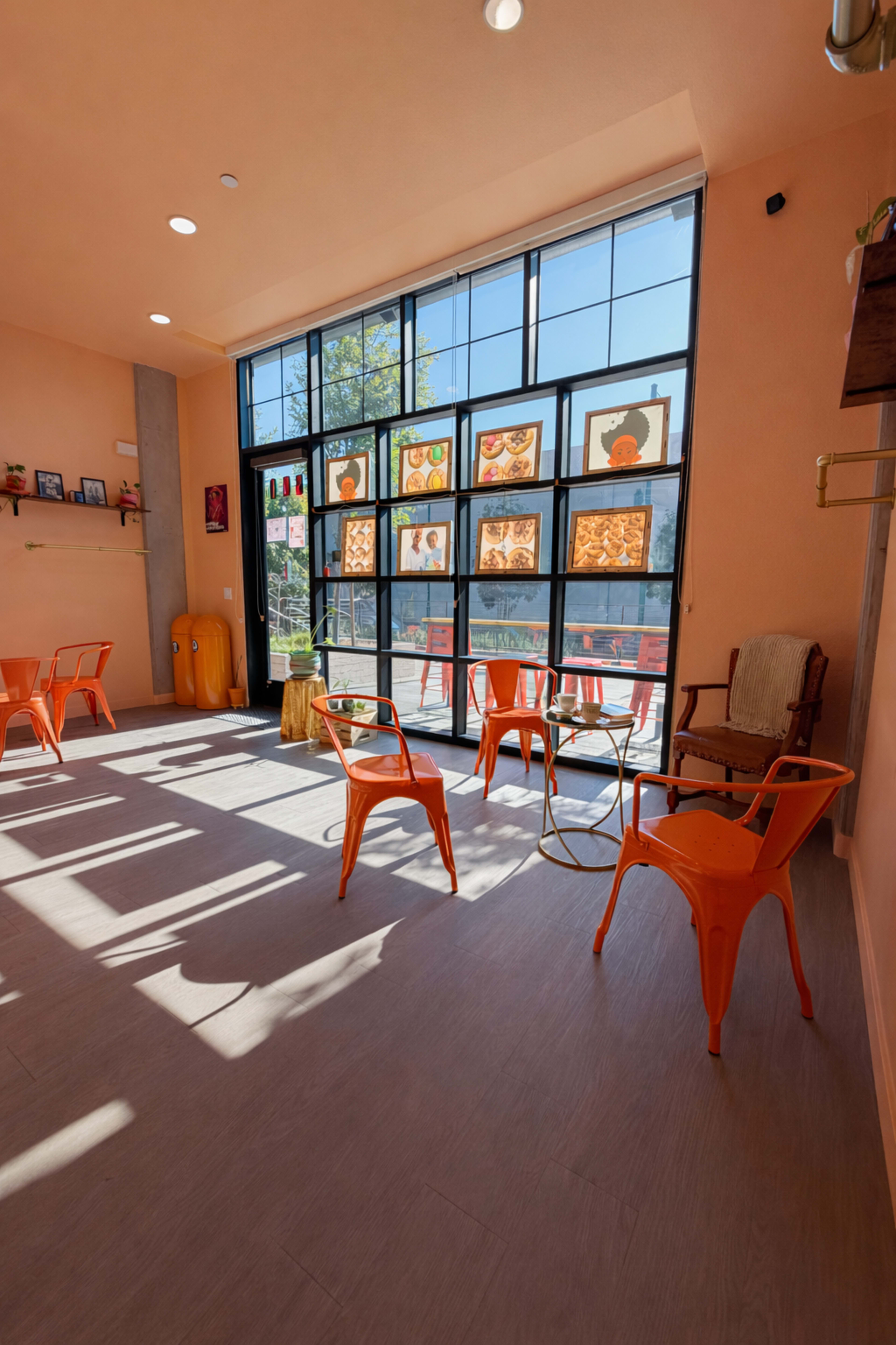 The image shows a cafe interior with orange chairs and large glass windows, allowing natural light to fill the space.